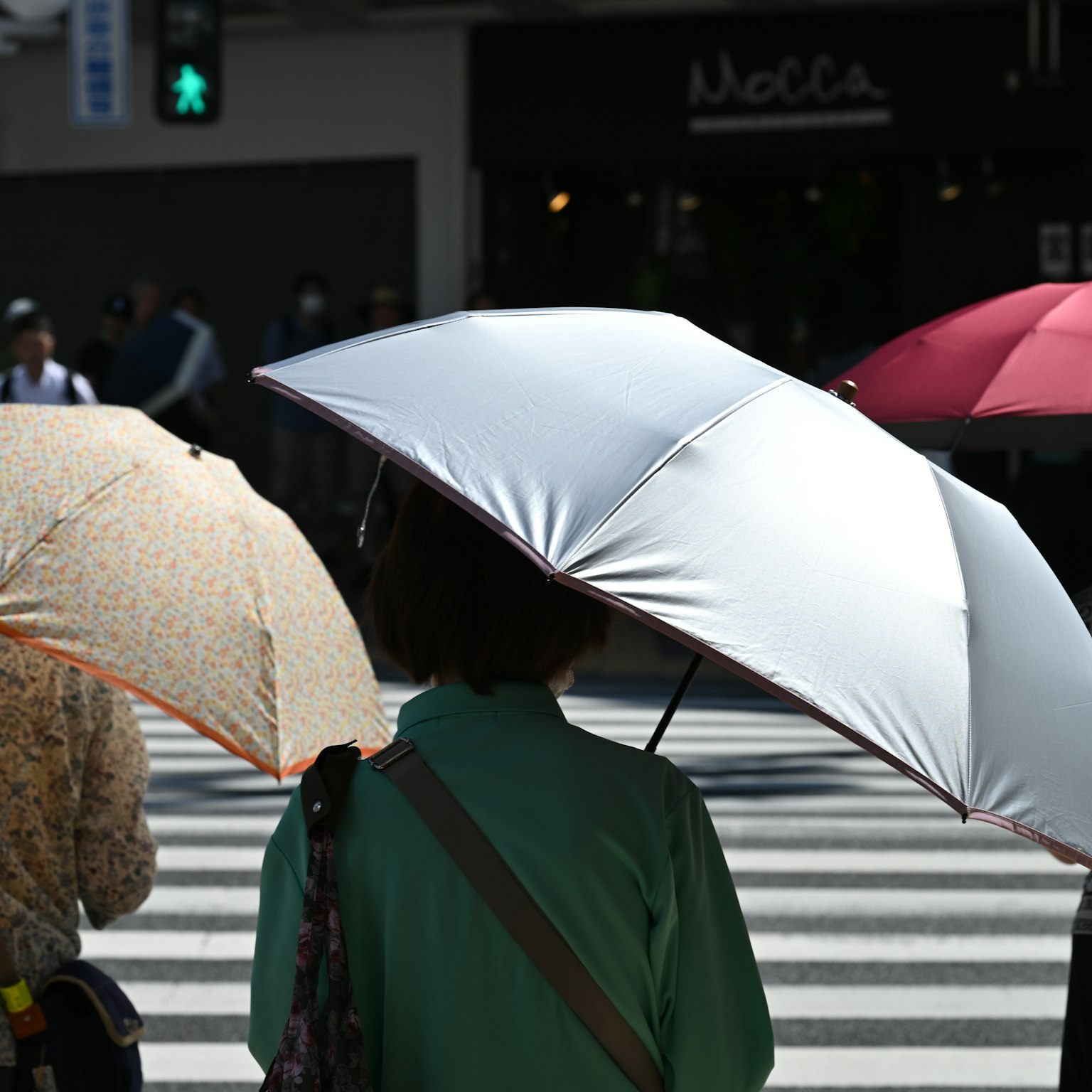 People crossing the street with umbrellas in a sunny setting