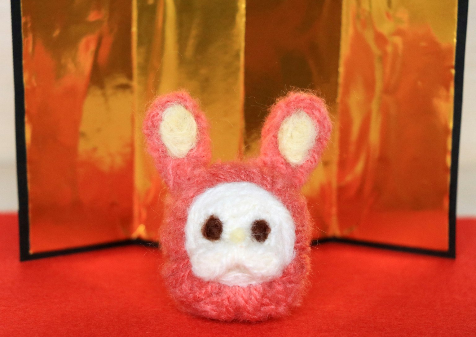 Un jouet en peluche de lapin rose exposé devant un fond doré
