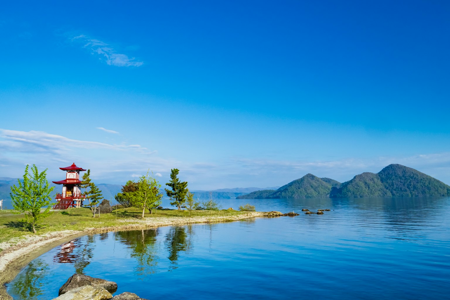 Scenic view of a lake with a small island and a red pagoda under a blue sky