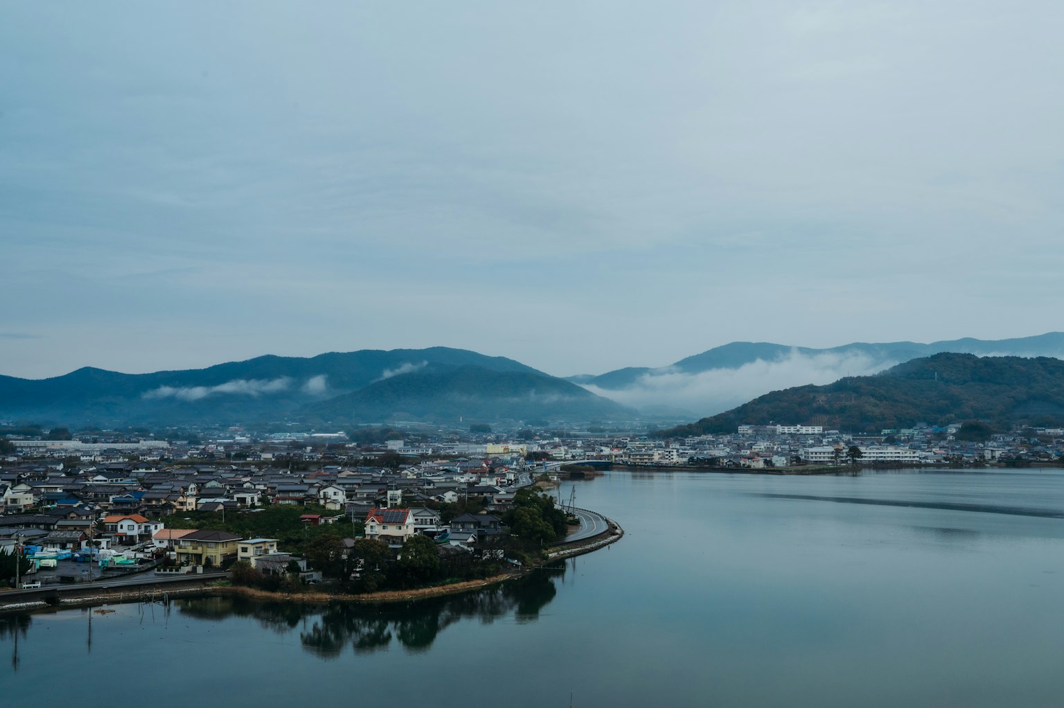 Pemandangan kota dengan teluk tenang dan pegunungan di latar belakang