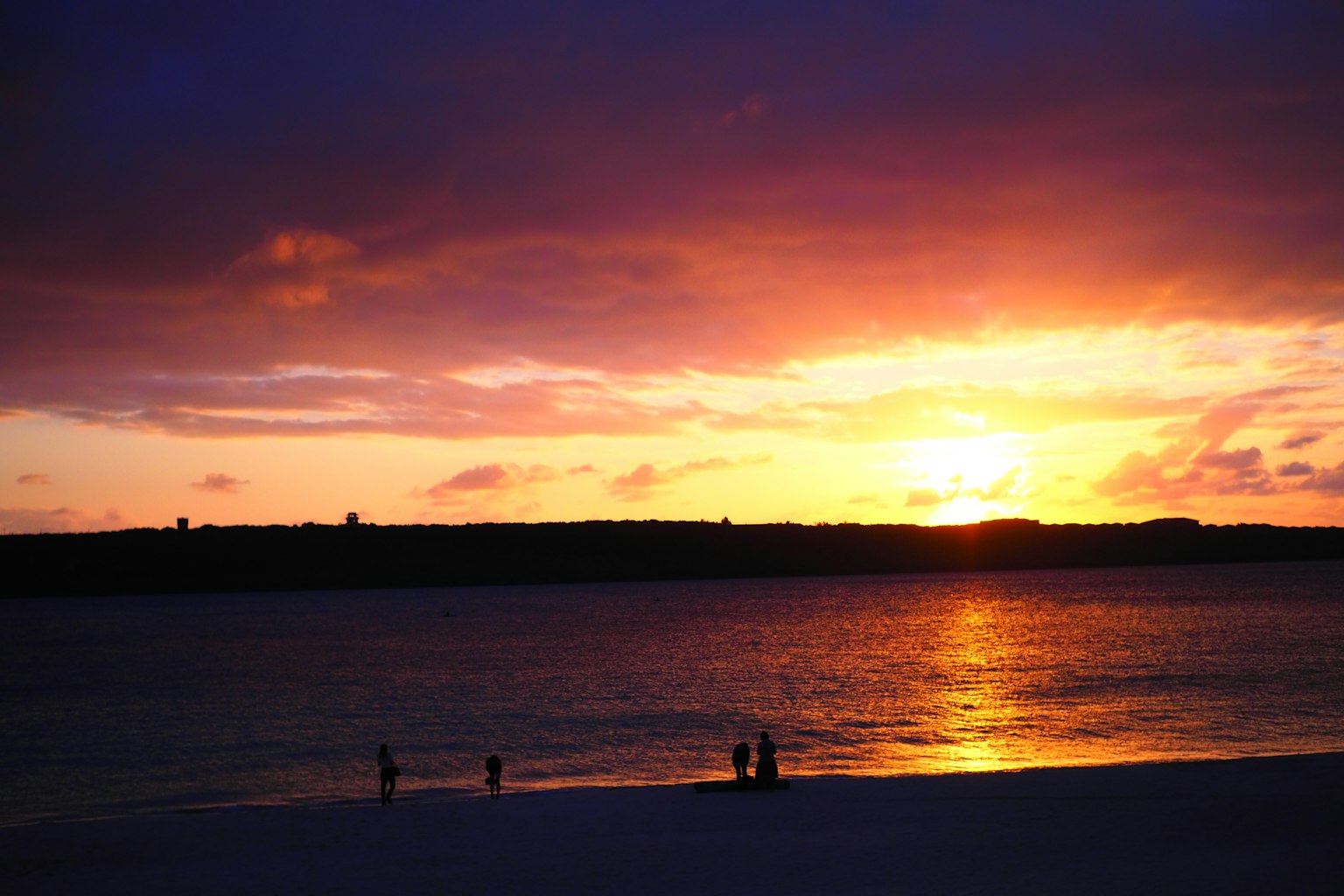 Silueta de personas en la playa al atardecer con un cielo vibrante de naranja y púrpura
