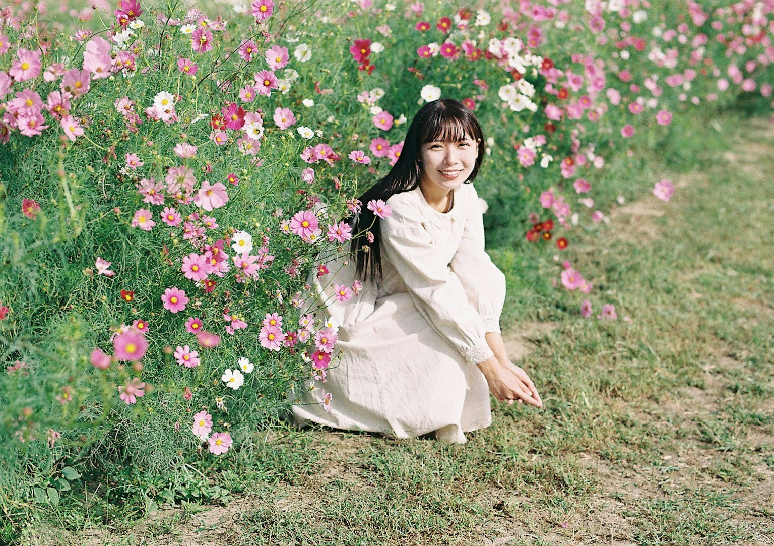 Une femme en robe blanche assise parmi des fleurs colorées