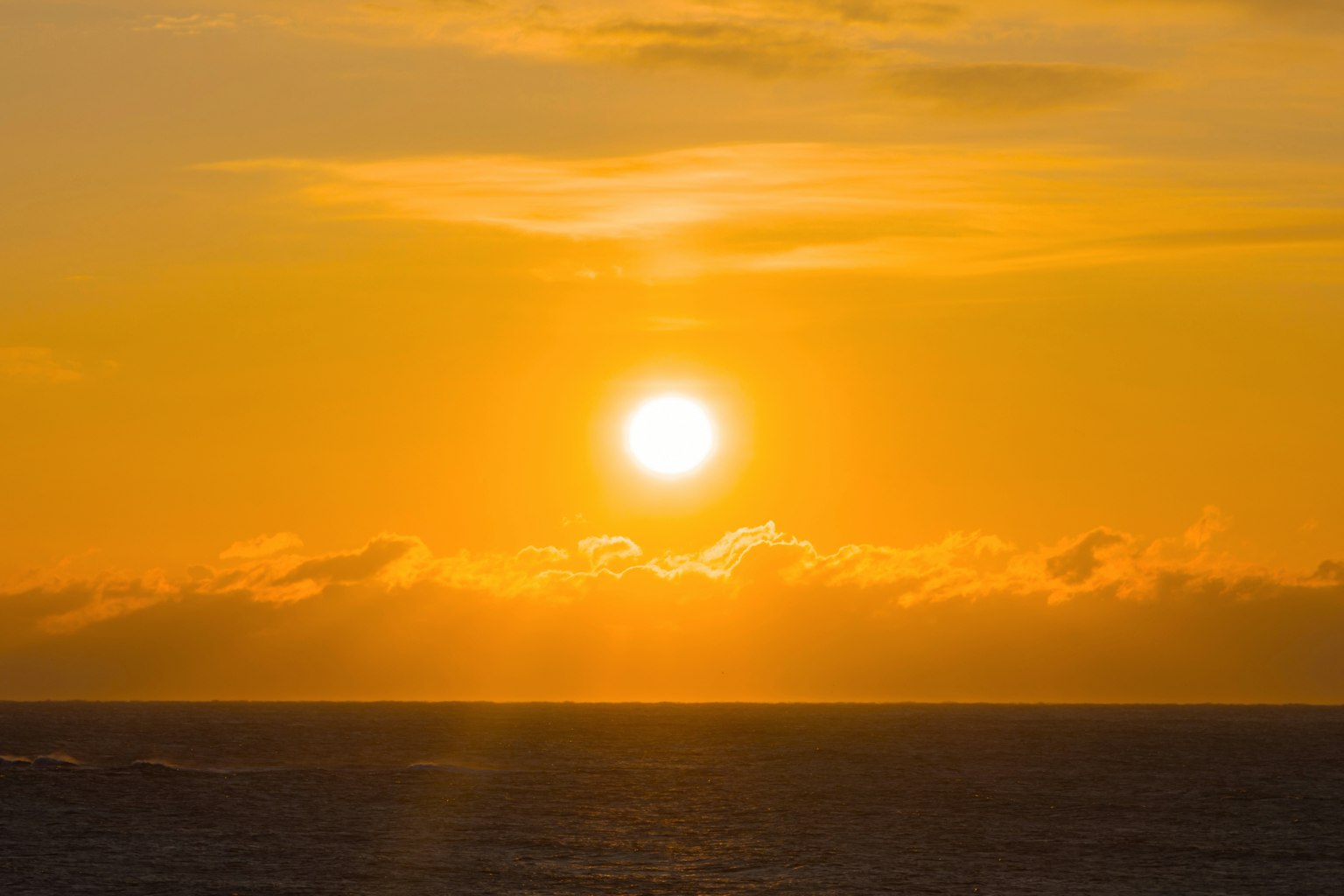 Sol naranja poniéndose sobre el océano con nubes