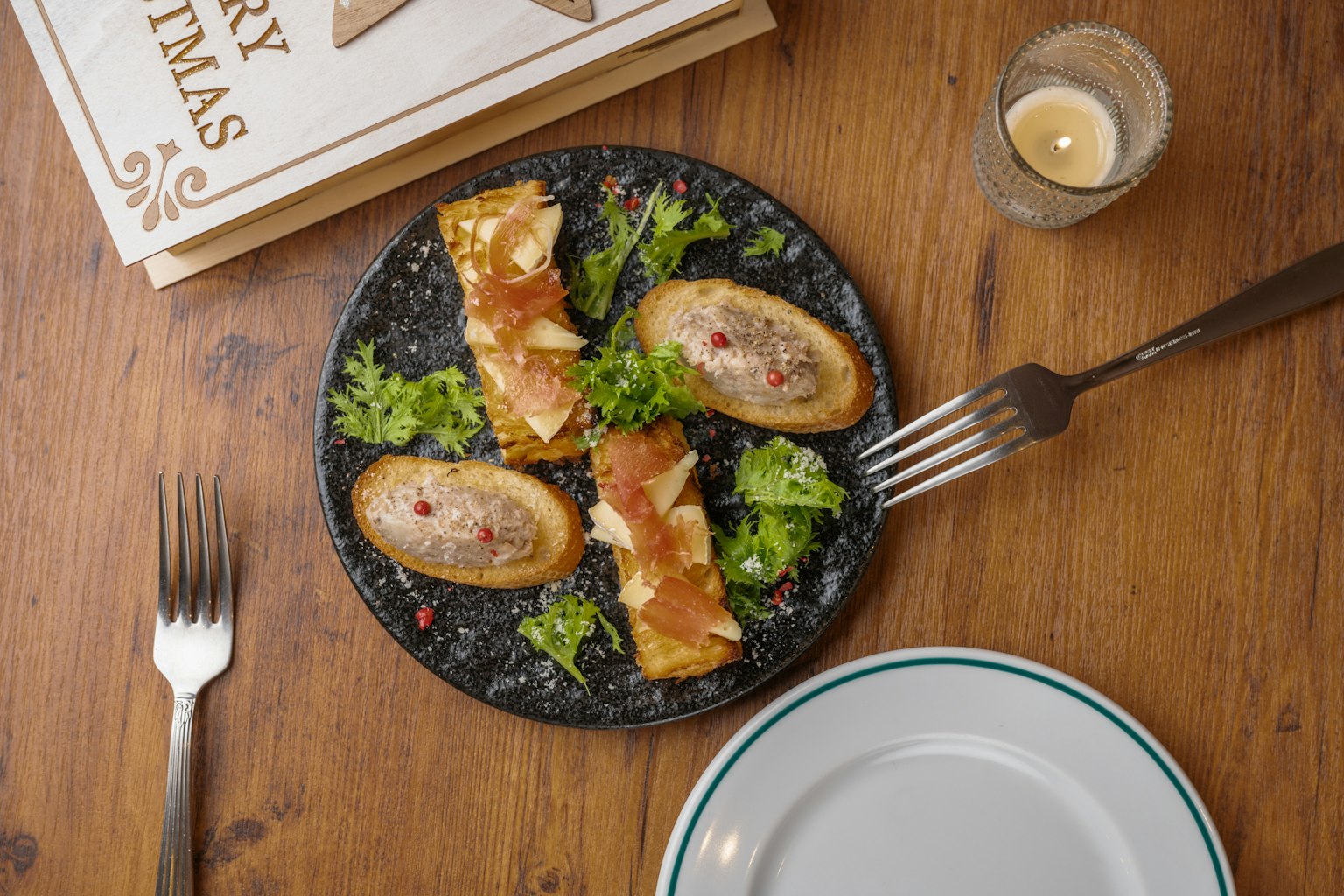 Une assiette avec une salade et des ingrédients disposés sur un plat noir Fourchette et couteau sur une table en bois