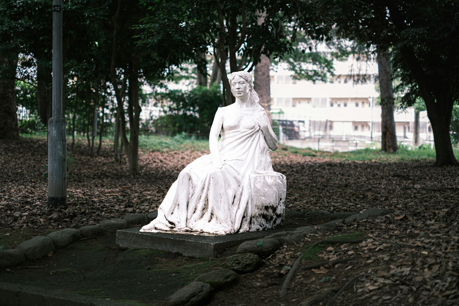 Una statua bianca seduta in un parco circondata da alberi verdi
