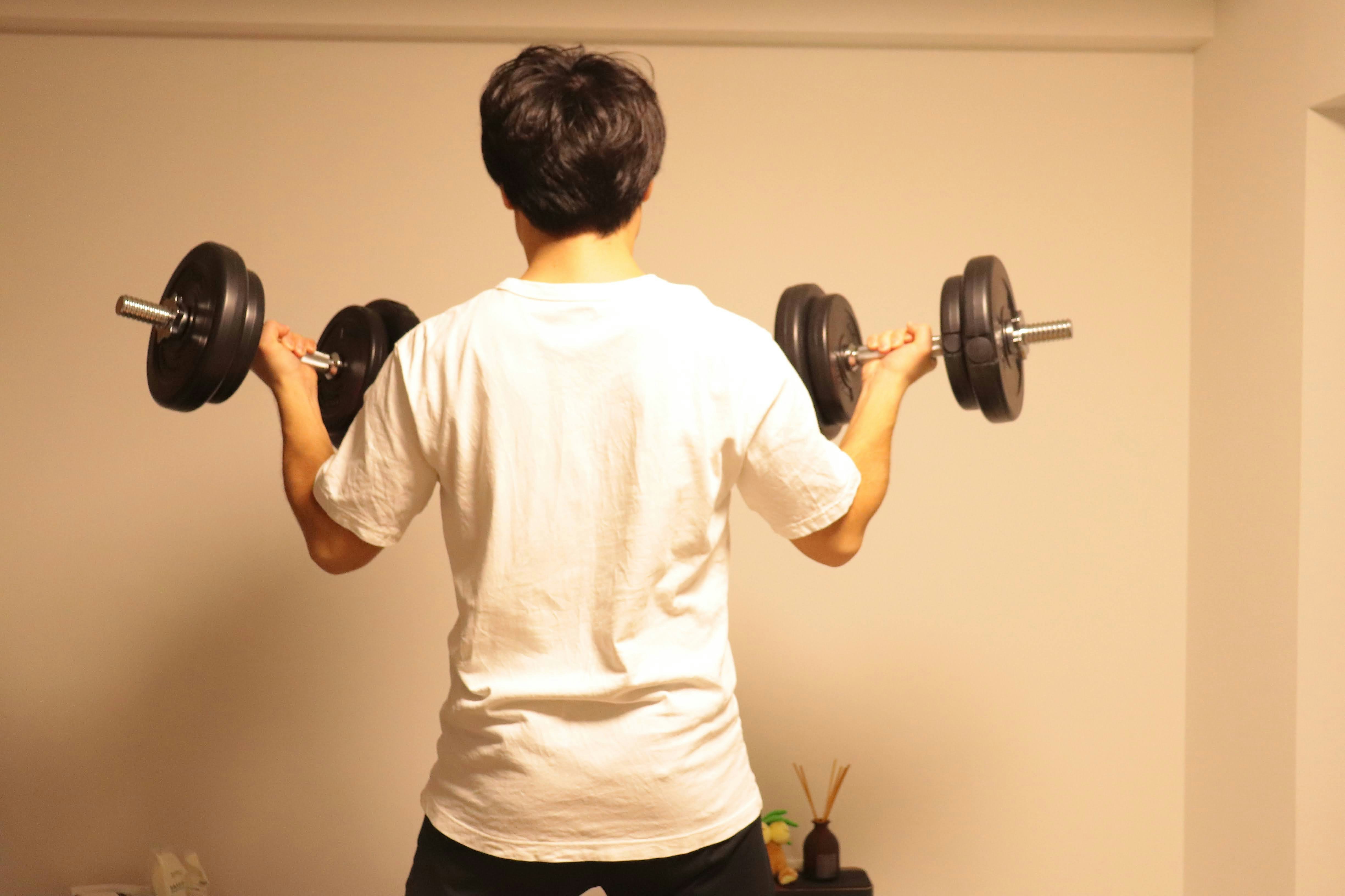 背中を見せてダンベルを持ち上げるトレーニング中の人物