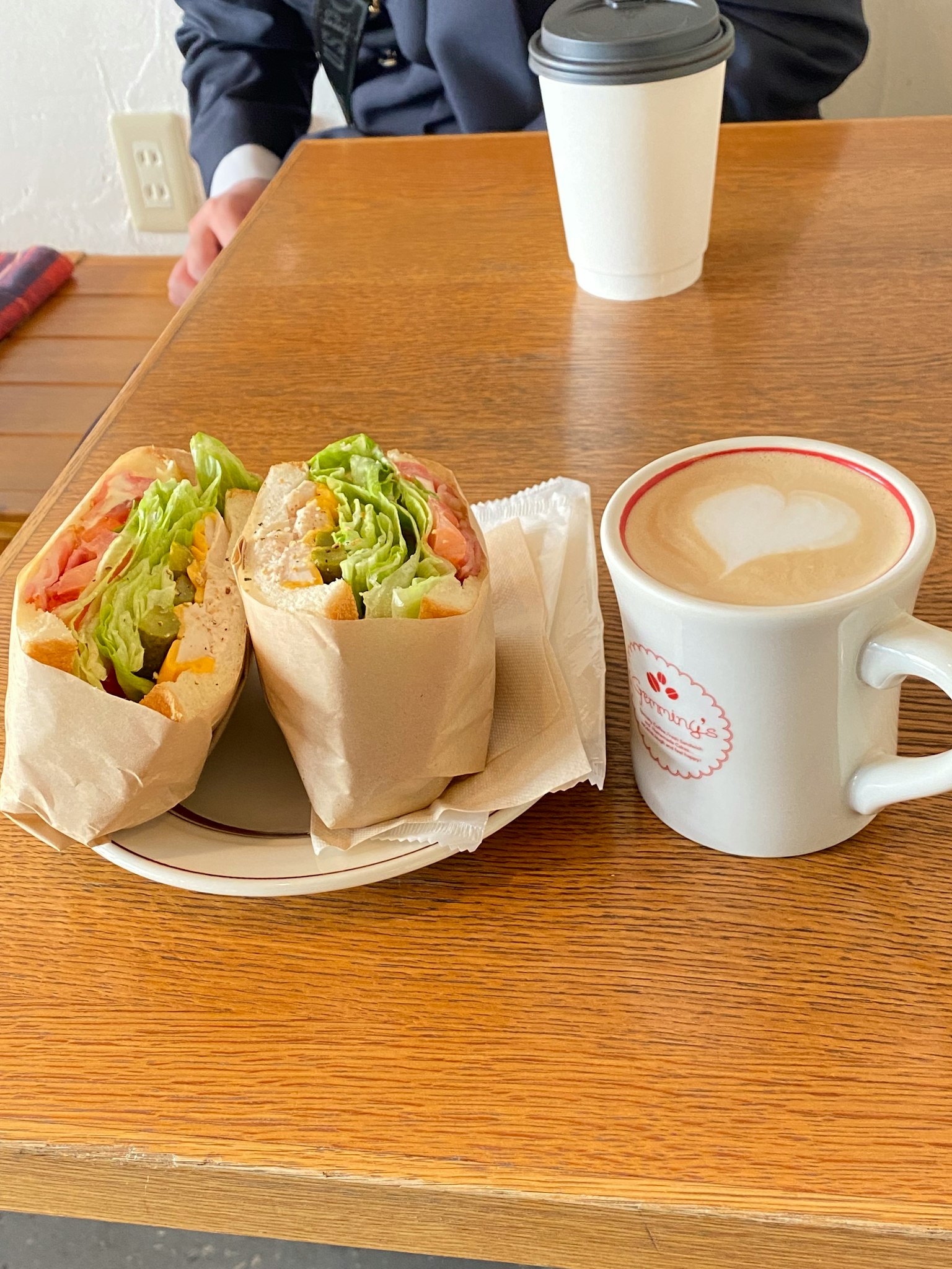 A cafe scene with a sandwich and a cup of coffee on a wooden table