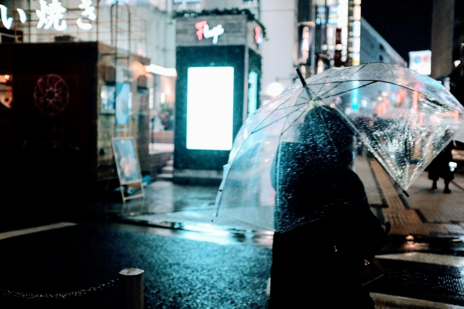 一個人在雨中撐著透明雨傘，背景是夜晚的城市燈光