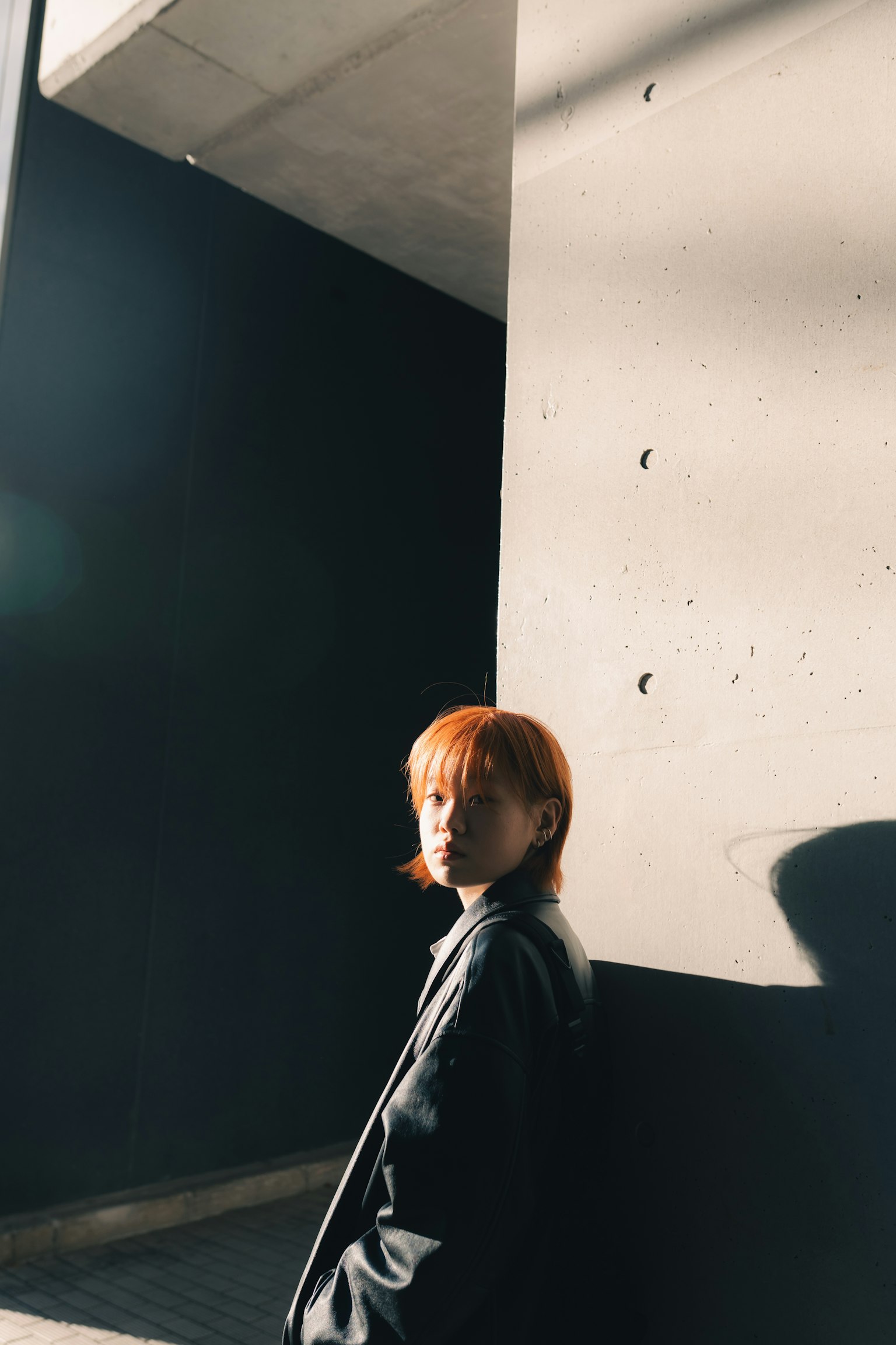 Retrato de una mujer pelirroja de pie frente a una pared de concreto Destacada por el contraste de luz y sombra