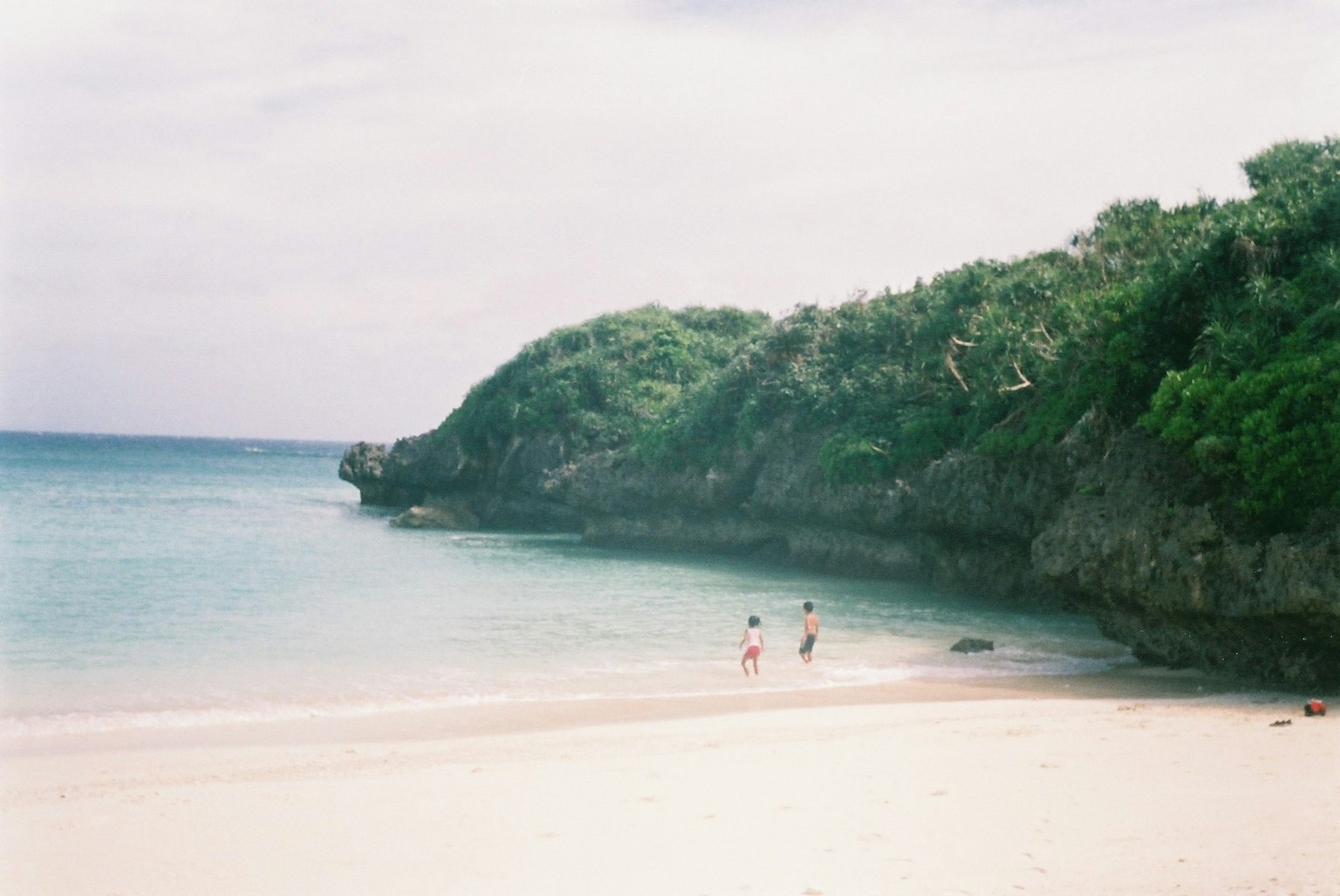 Scena di una spiaggia con acqua blu e sabbia bianca dove tre persone camminano