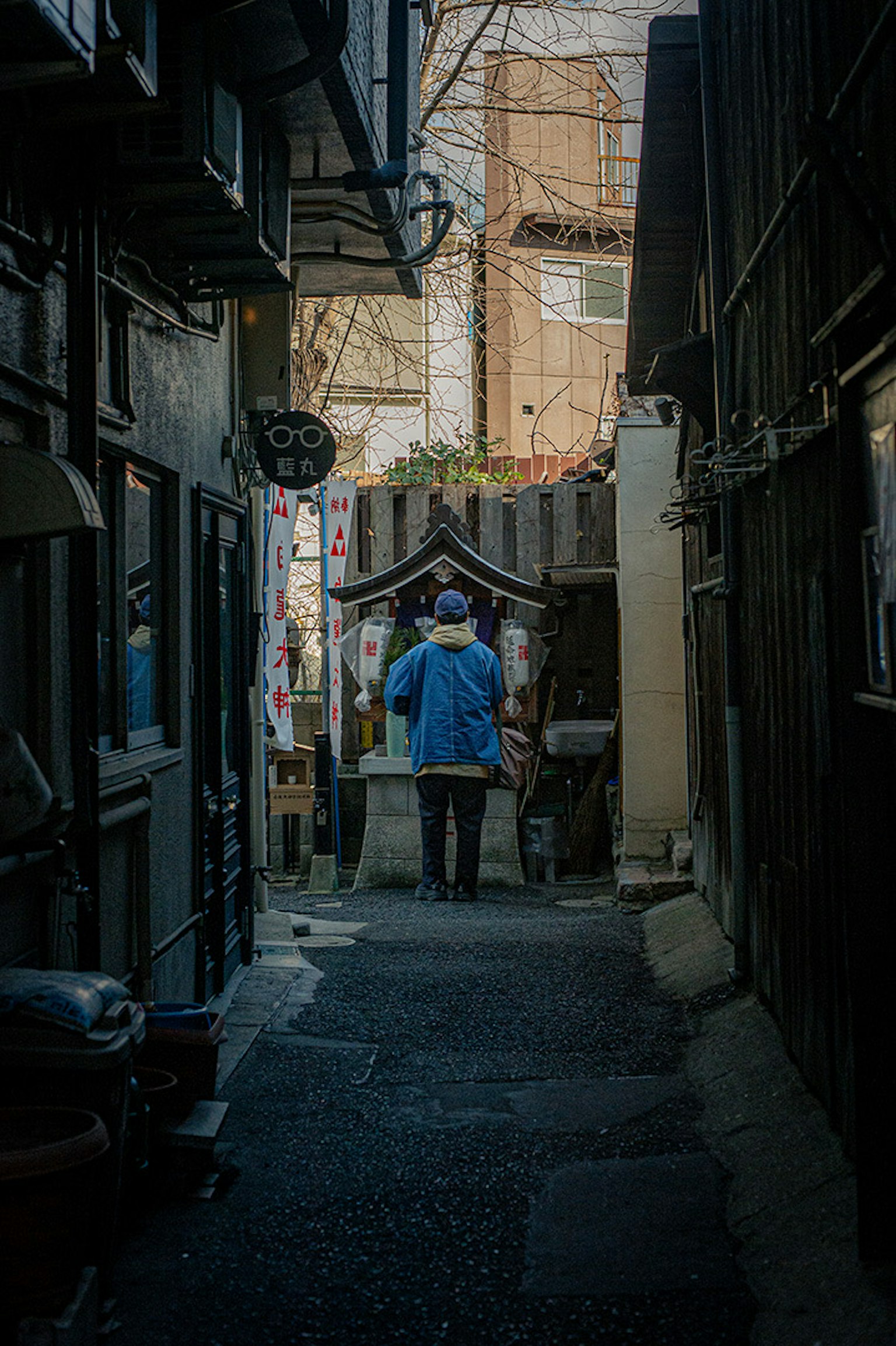 一个穿蓝色衣服的人站在狭窄的小巷中，背景是一座神社