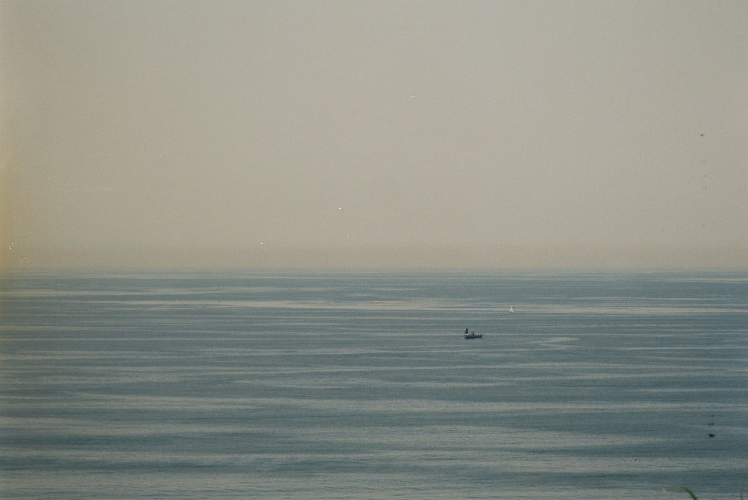 Calm sea landscape with a small boat on a light blue horizon