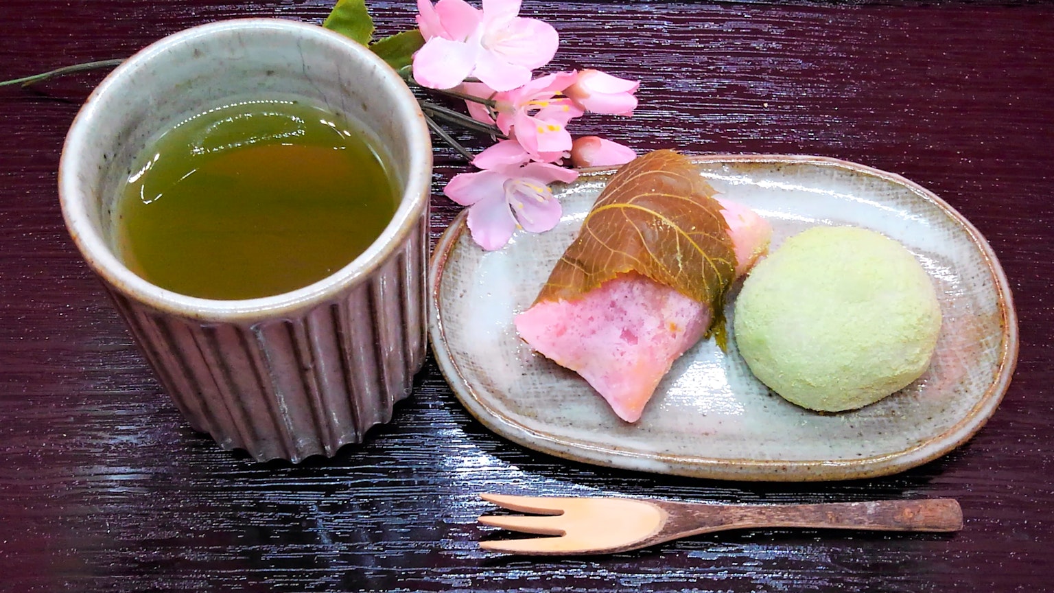 Thé vert et sucreries japonaises présentés sur une assiette en céramique avec des fleurs de cerisier