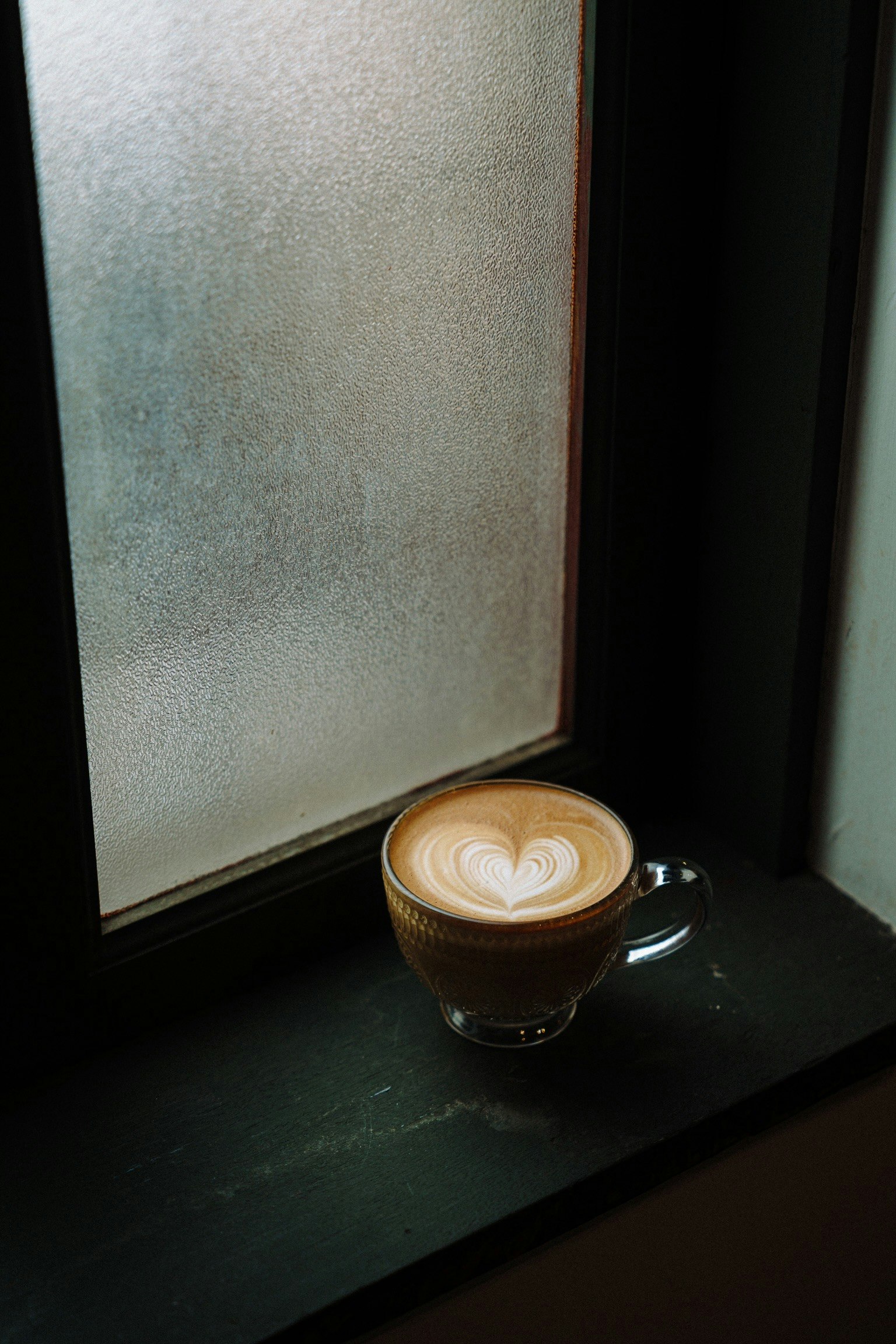 Tasse de latte avec un motif en forme de cœur sur le rebord d'une fenêtre