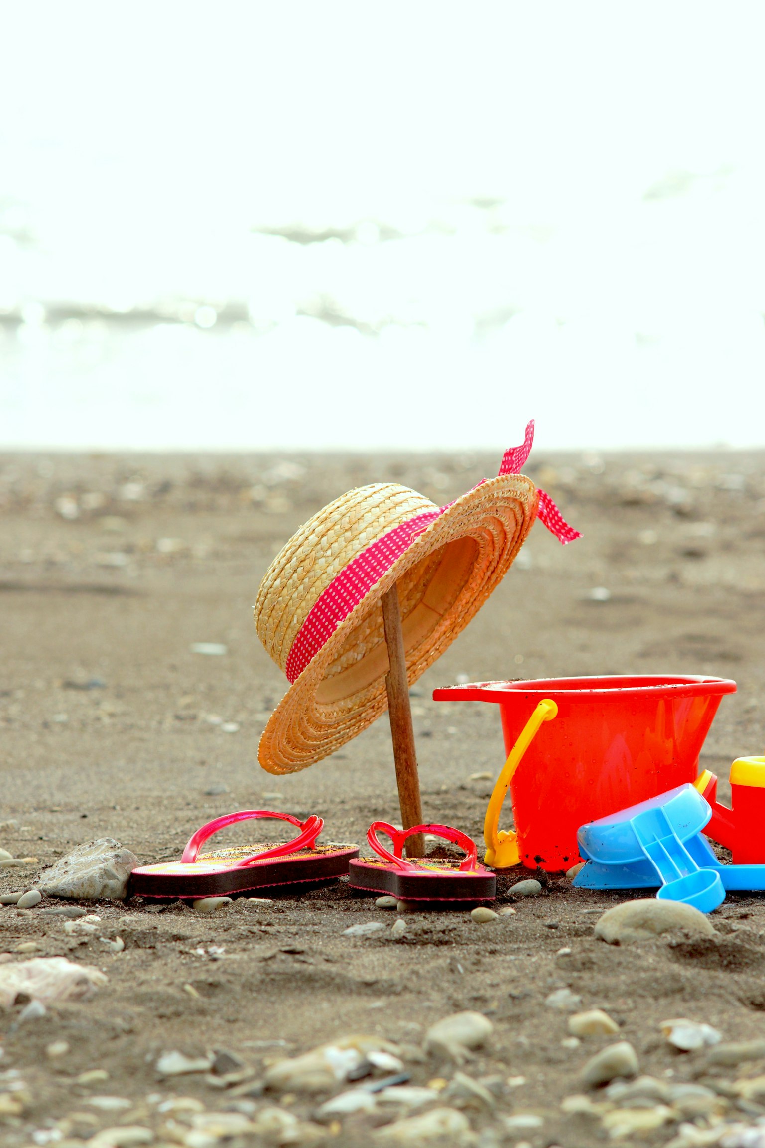 Topi jerami dan mainan pantai di pasir dekat pantai