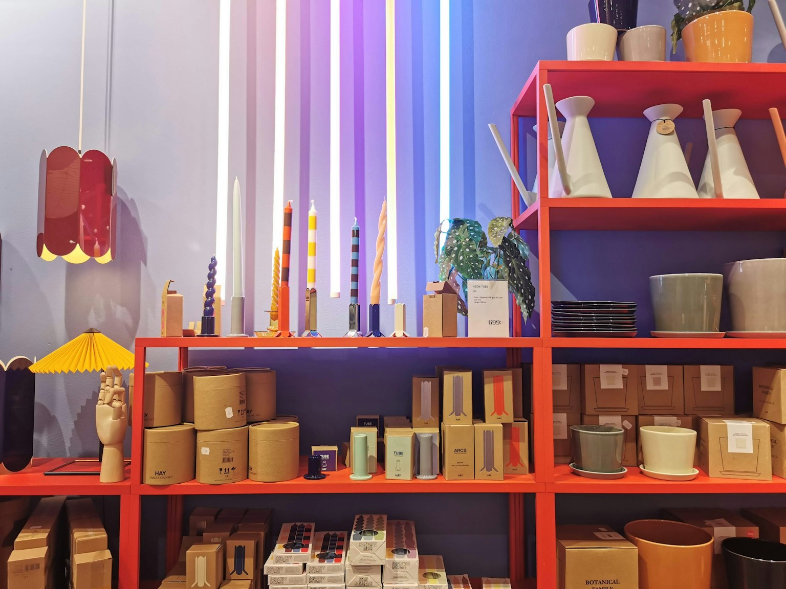 Articles de décoration intérieure colorés exposés sur une étagère rouge avec des lumières vives au-dessus