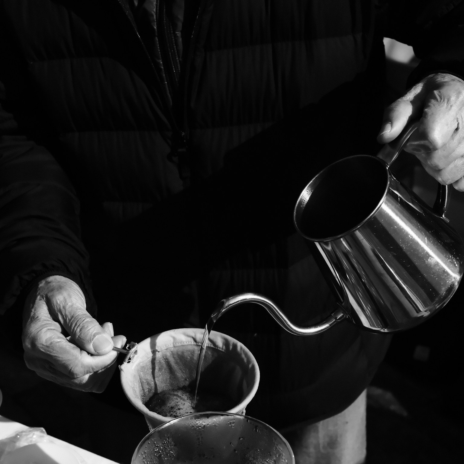 コーヒーを注ぐ手元の写真 銀色のポットからコーヒーが注がれている