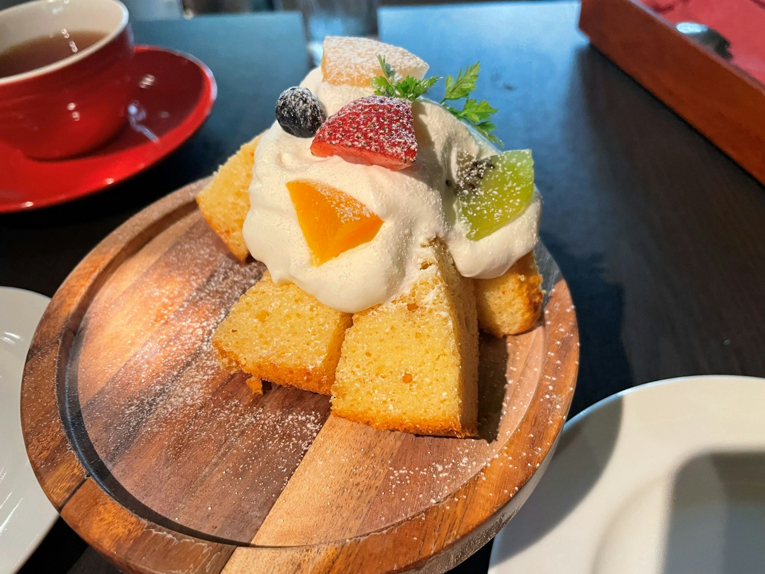 一片蛋糕,上面放着五颜六色的水果和奶油,放在木盘上