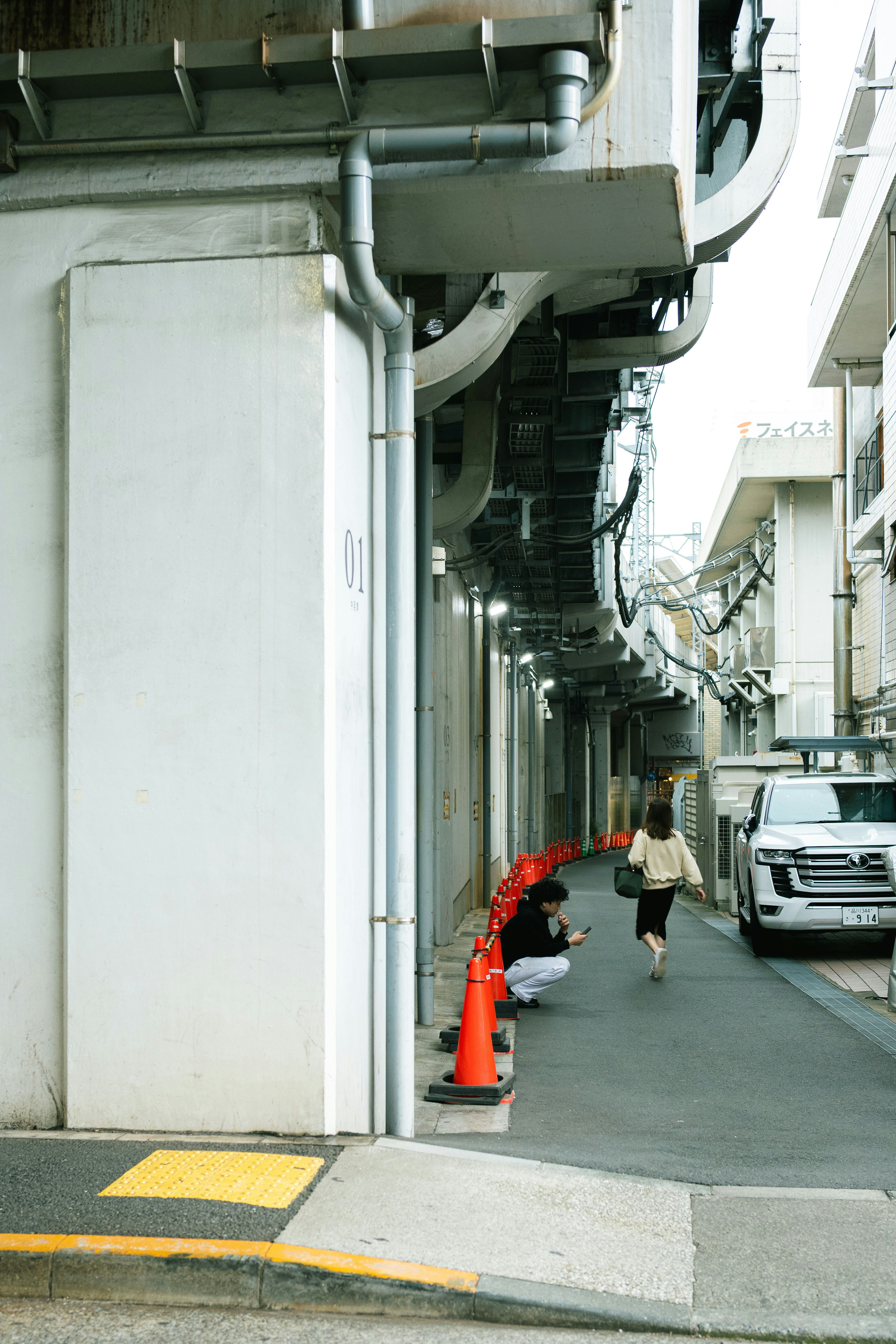 Street view with white buildings and orange cones along a narrow sidewalk