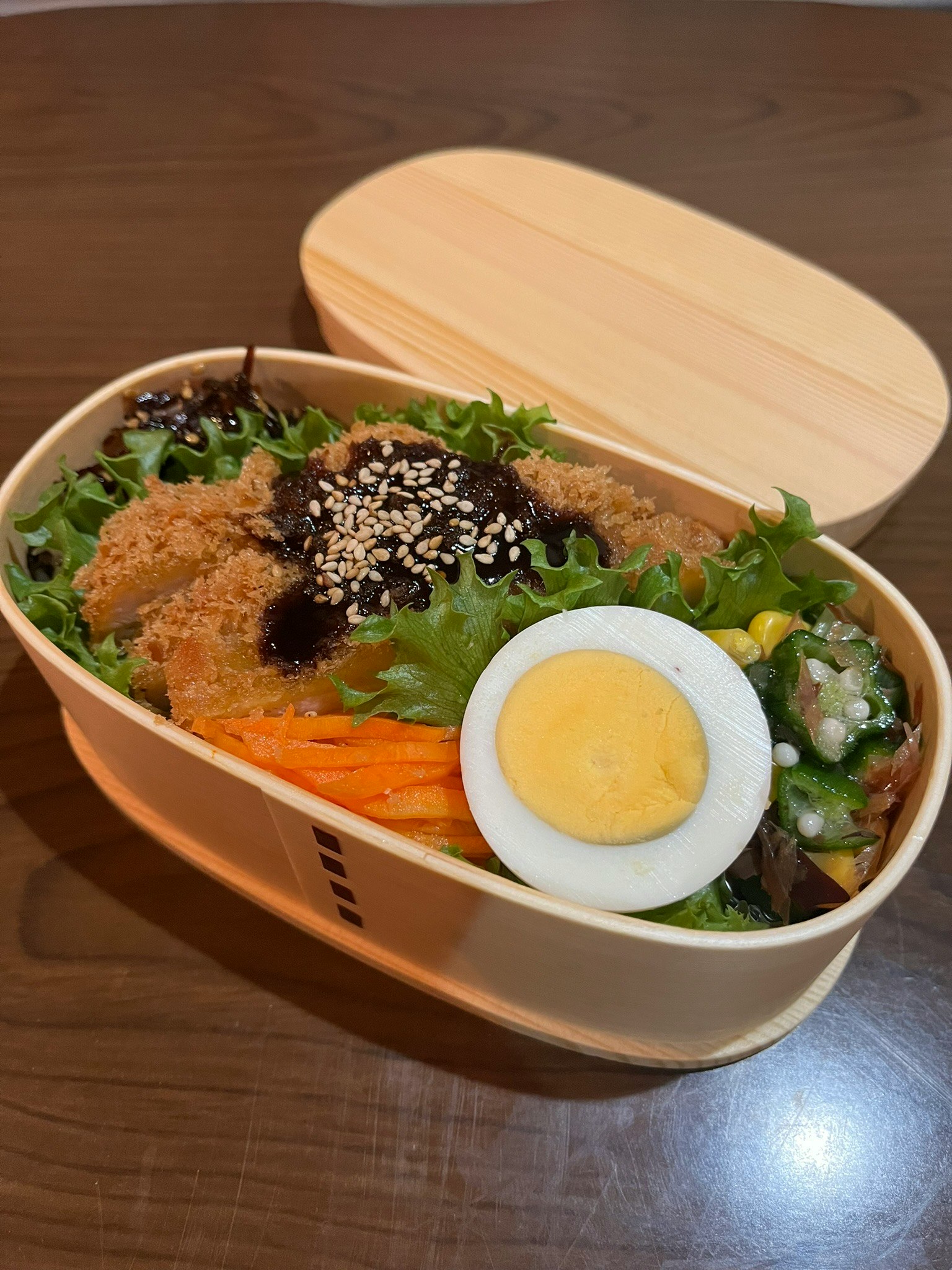 Une boîte à bento remplie de poulet frit et de légumes Riz garni de graines de sésame noir Un œuf dur coupé en deux est inclus