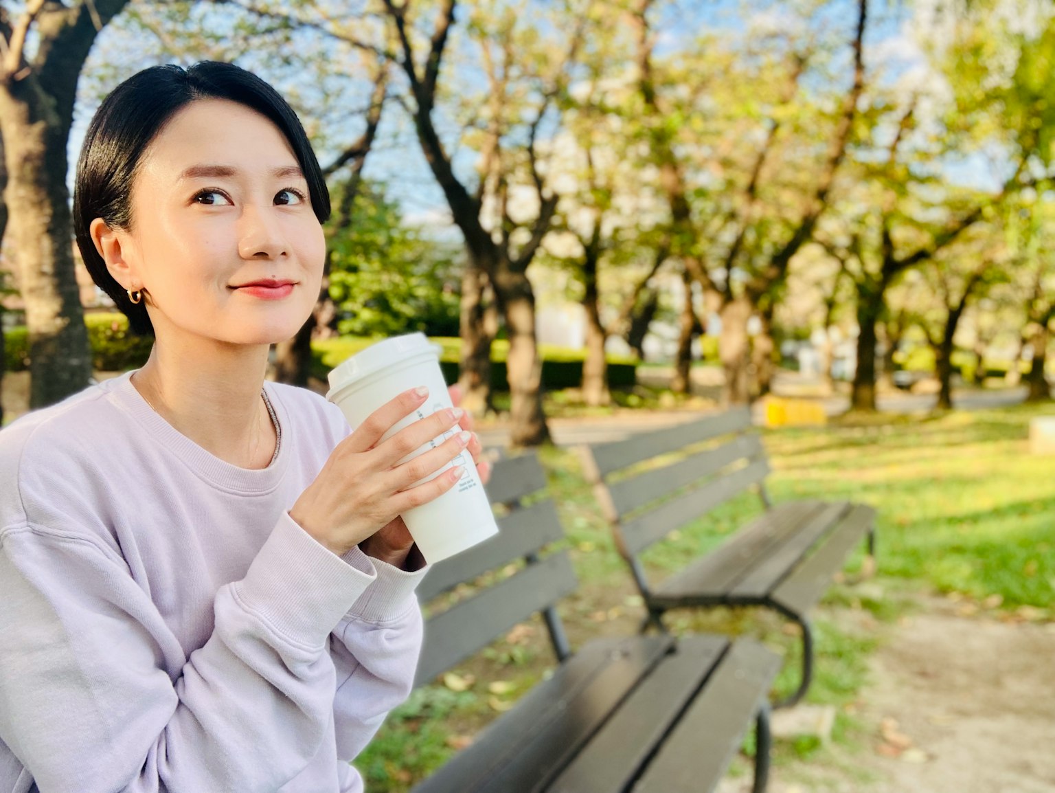공원 벤치에 앉아 커피컵을 들고 미소 짓고 있는 여성