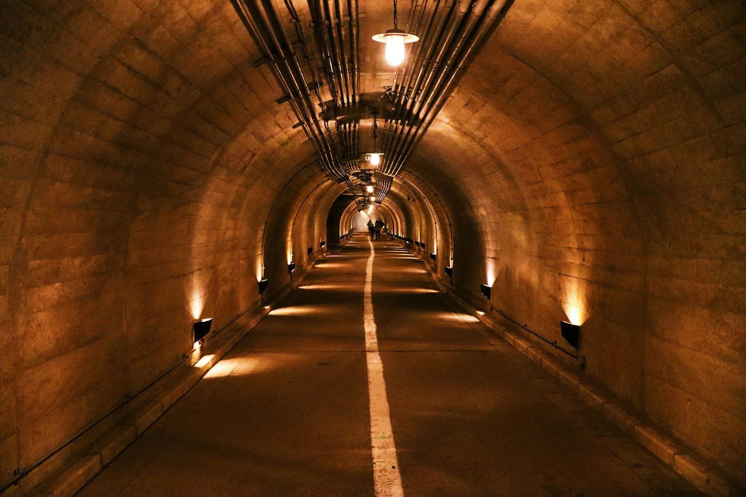 Tunnel éclairé avec une bande blanche centrale et des murs en pierre