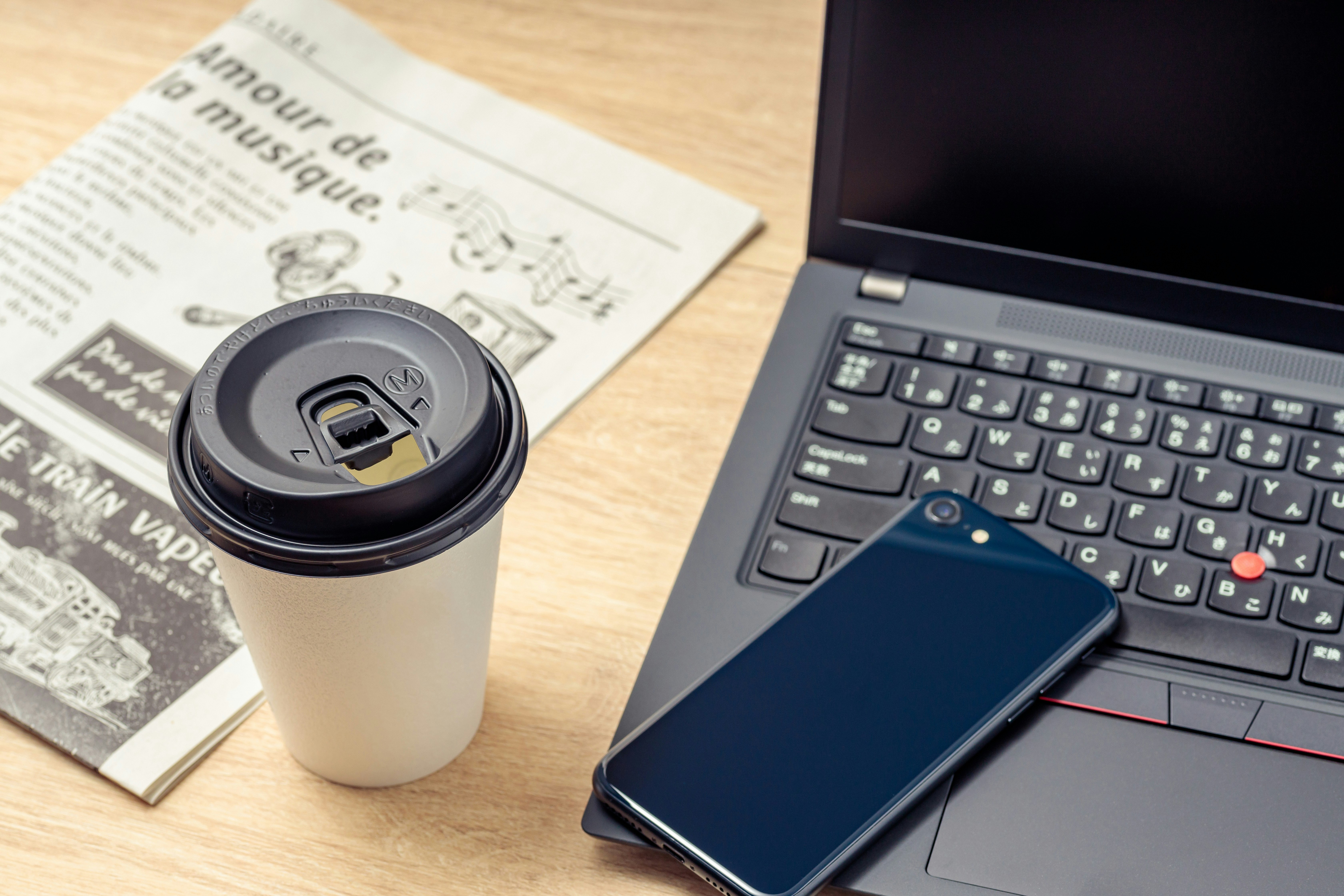 コーヒーと新聞、ノートPCとスマホが並ぶビジネスデスク