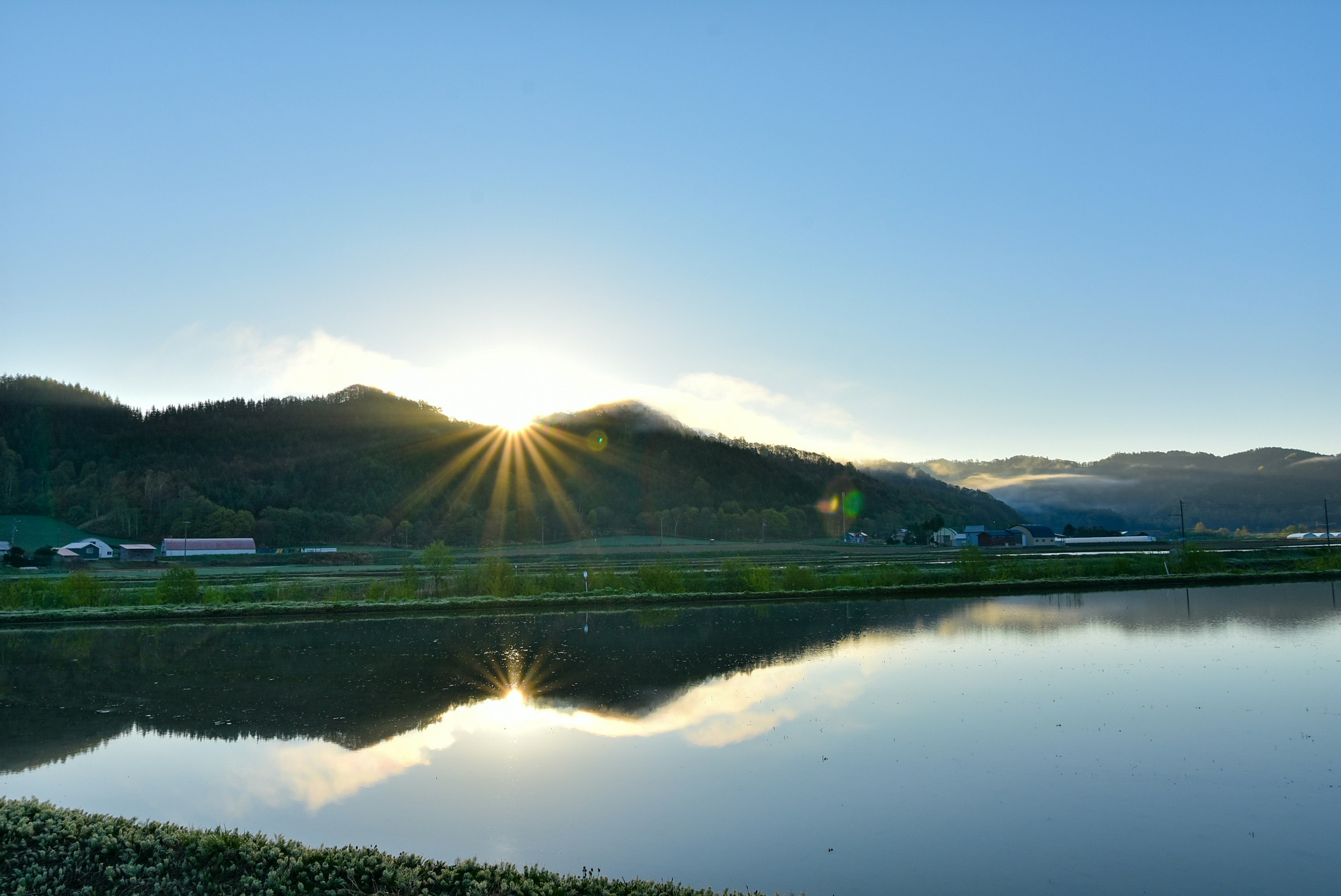 Sonnenaufgang über einem ruhigen See mit Spiegelung der Berge