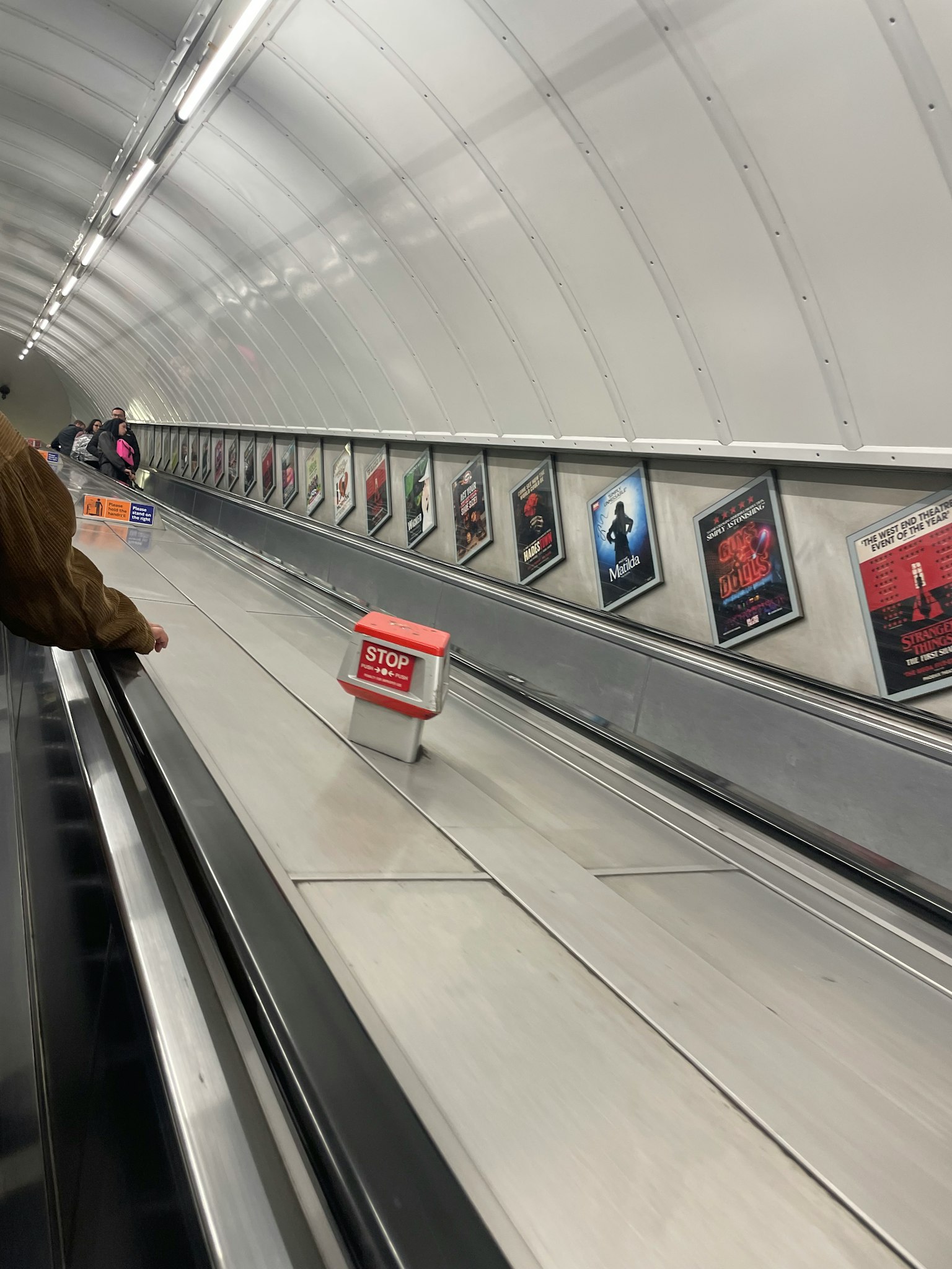 Subway escalator with advertisements lining a white tunnel