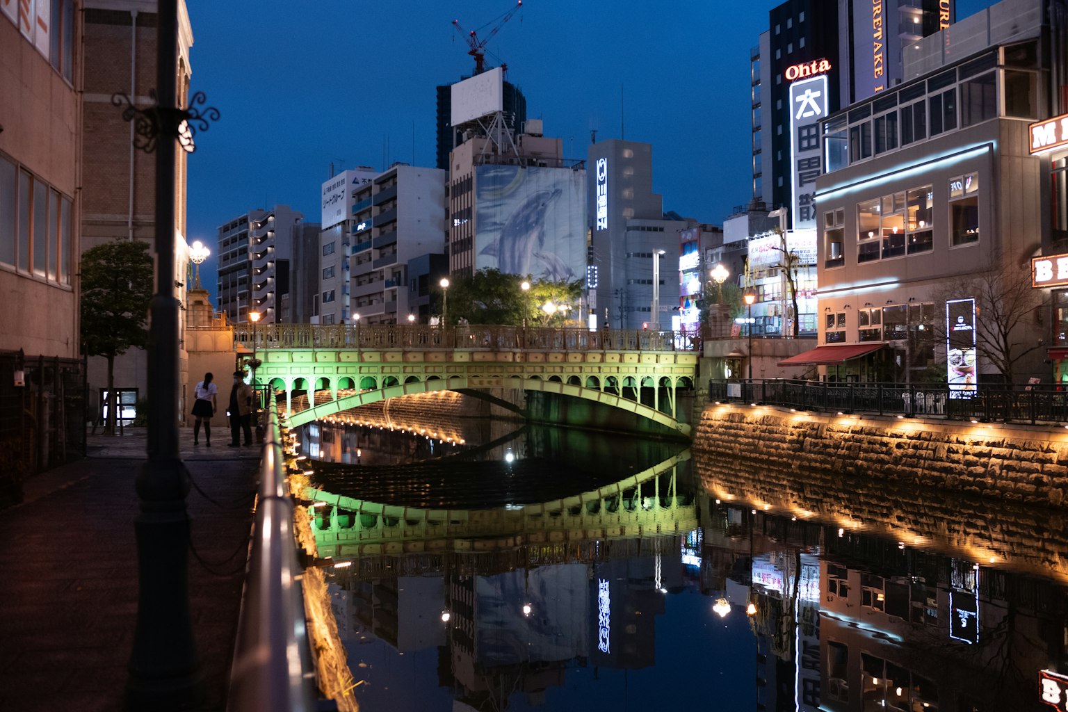 ทิวทัศน์ยามค่ำคืนของเมืองที่มีสะพานสีเขียวเหนือแม่น้ำที่สะท้อน