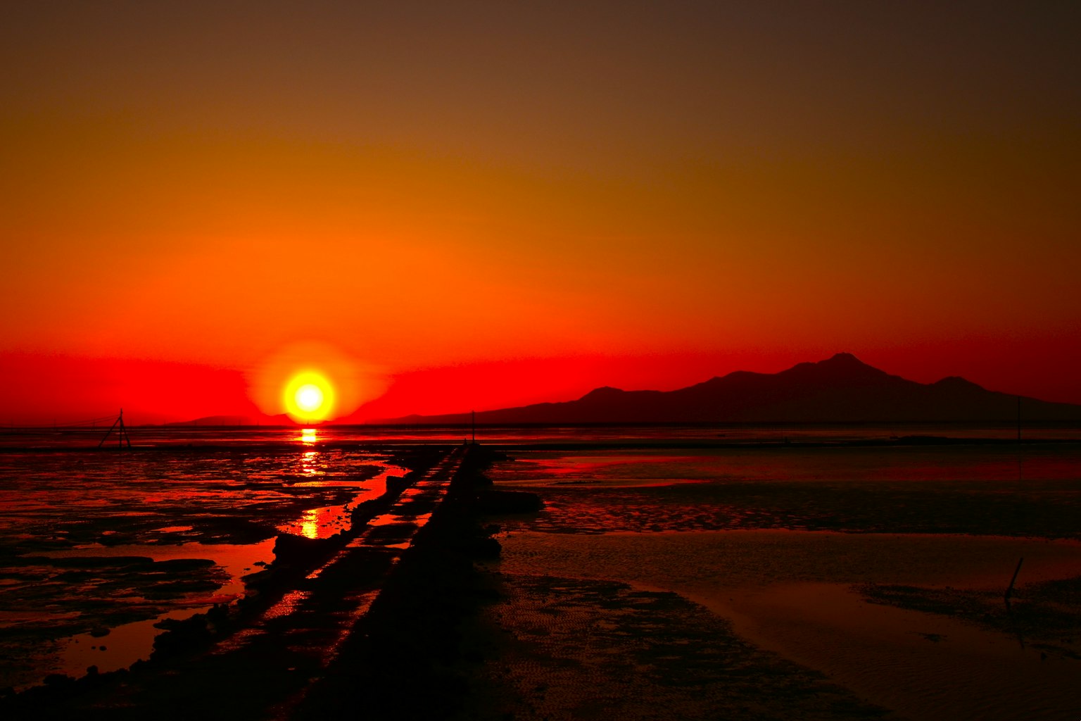 Un coucher de soleil rouge vif sur l'océan se reflétant dans les eaux calmes