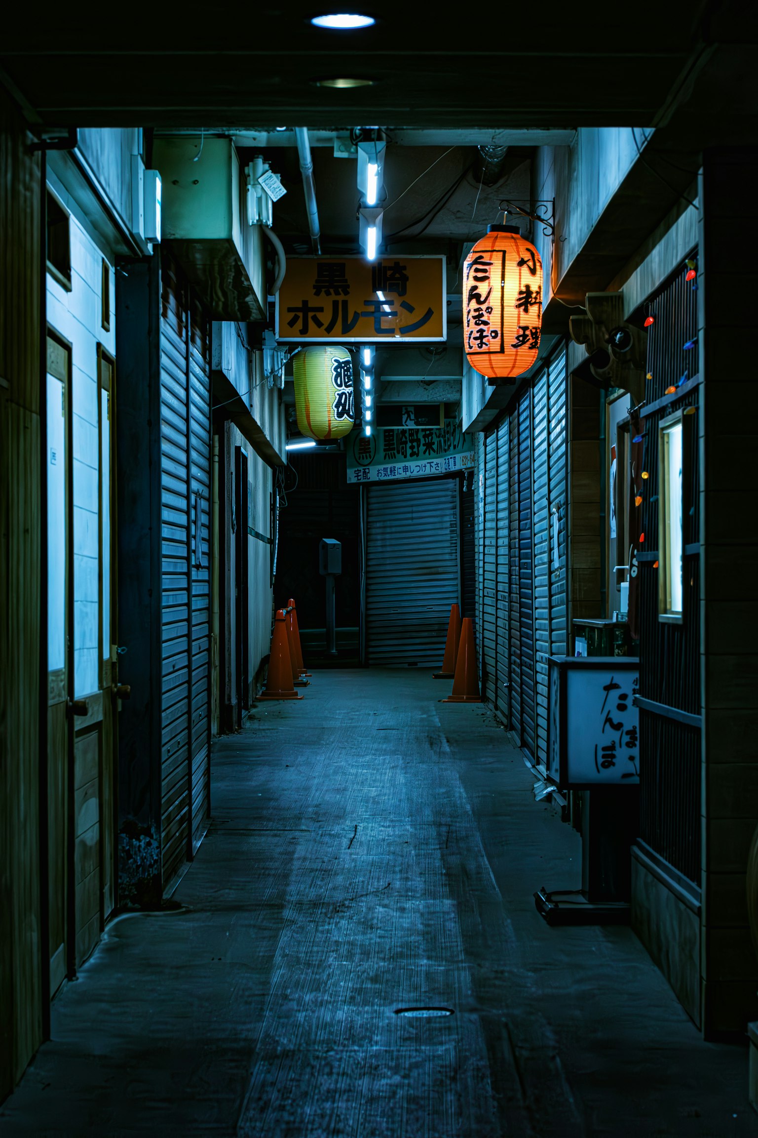 Vicolo poco illuminato con serrande chiuse e lanterne luminose