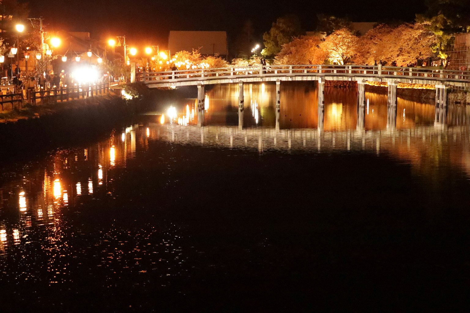 Pemandangan malam yang indah sungai dan jembatan dengan lampu jalan oranye yang memantul di air