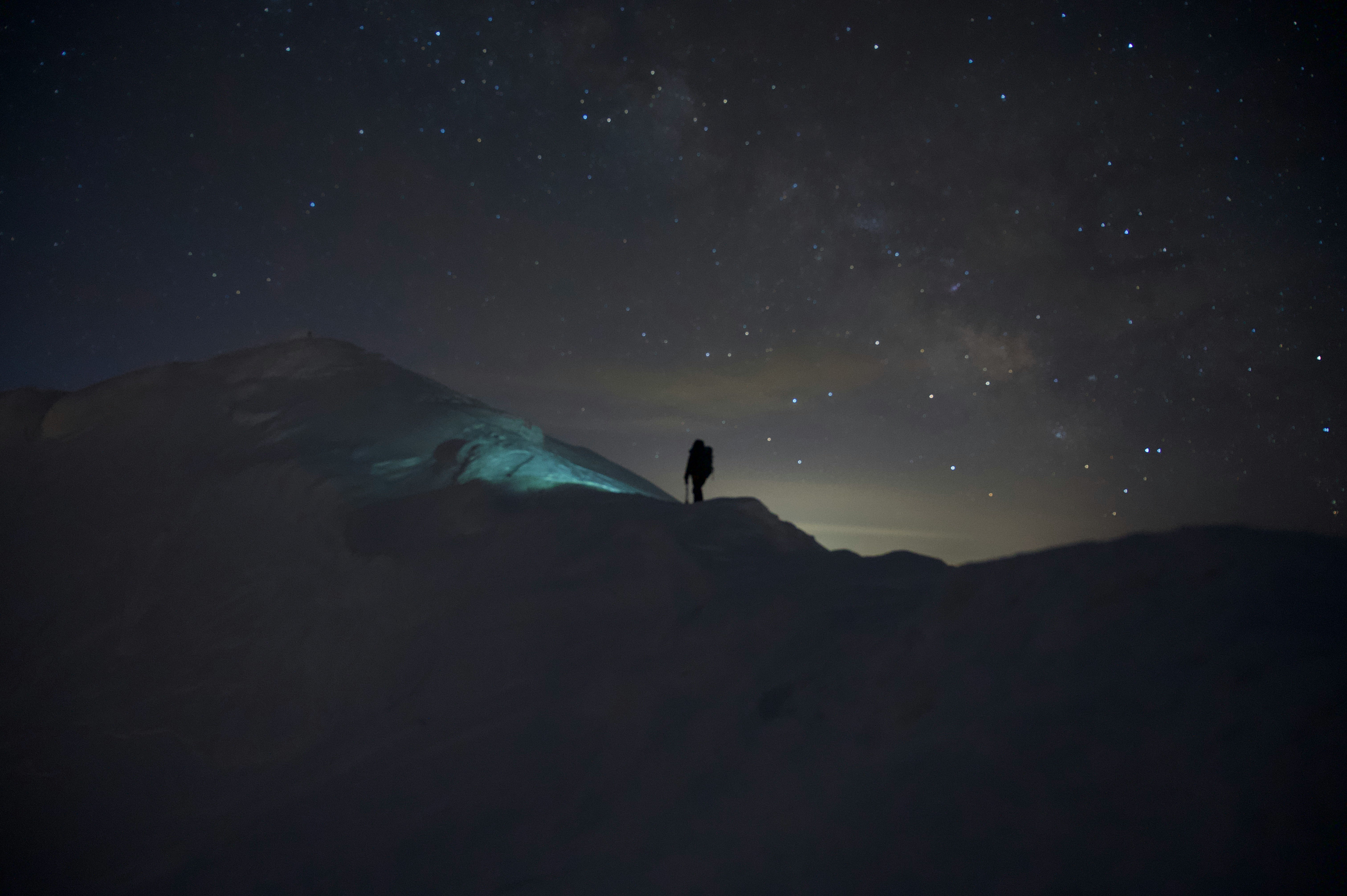 夜空の星と山の稜線に立つ一人の人物
