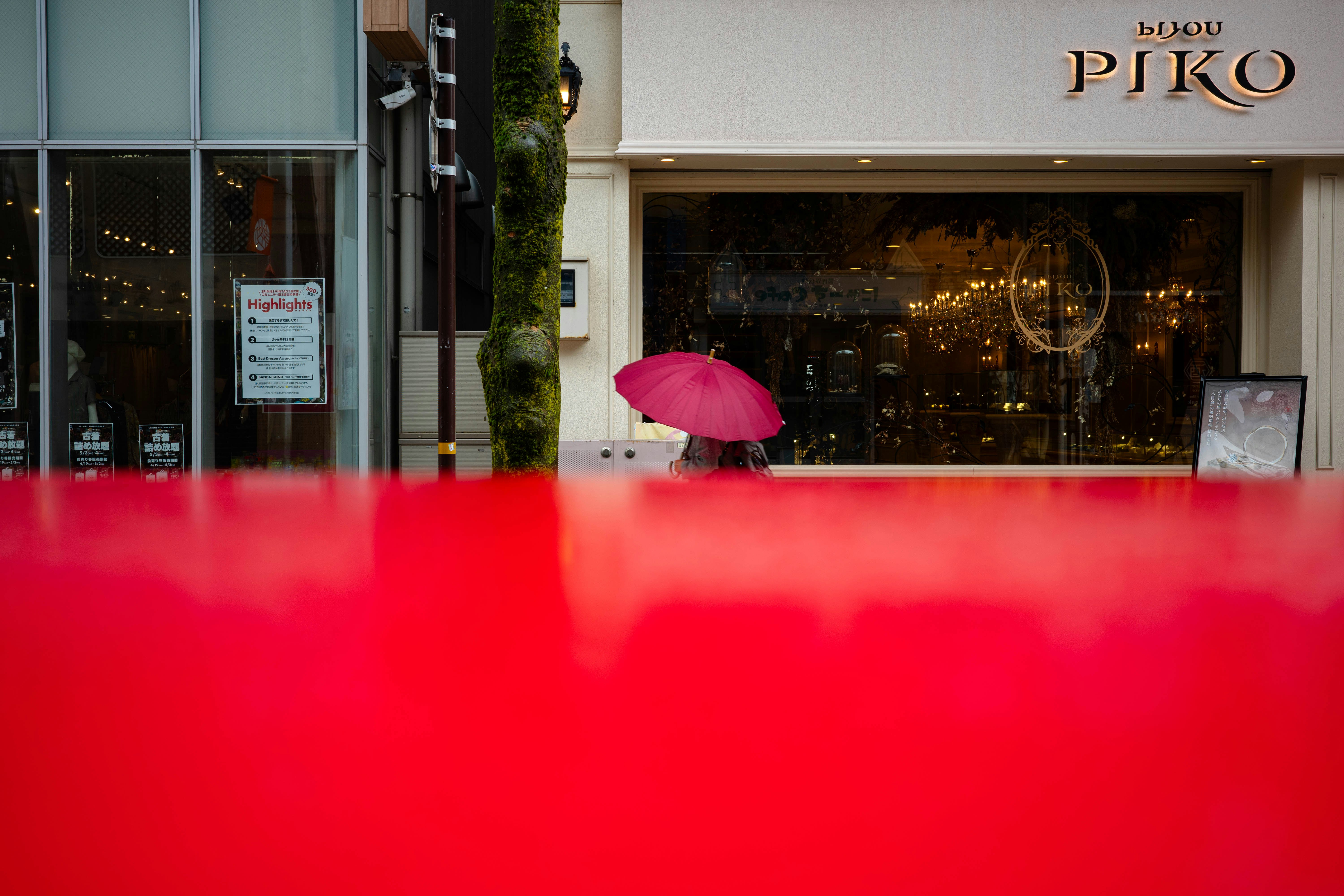 Angolo di strada con vetrina e ombrello rosa dietro un primo piano rosso
