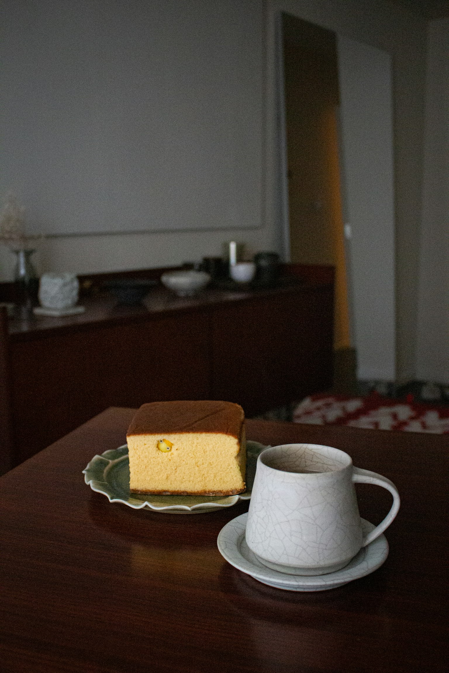A simple setting featuring a slice of cake on a plate and a cup of coffee on a wooden table