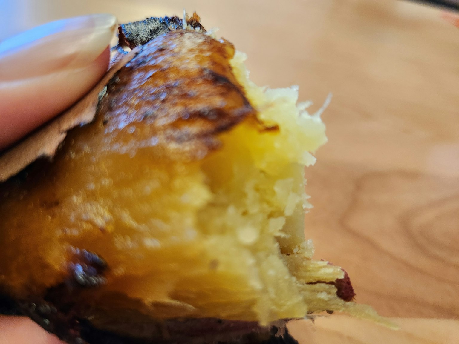 Close-up of baked sweet potato being held showing charred exterior and soft interior