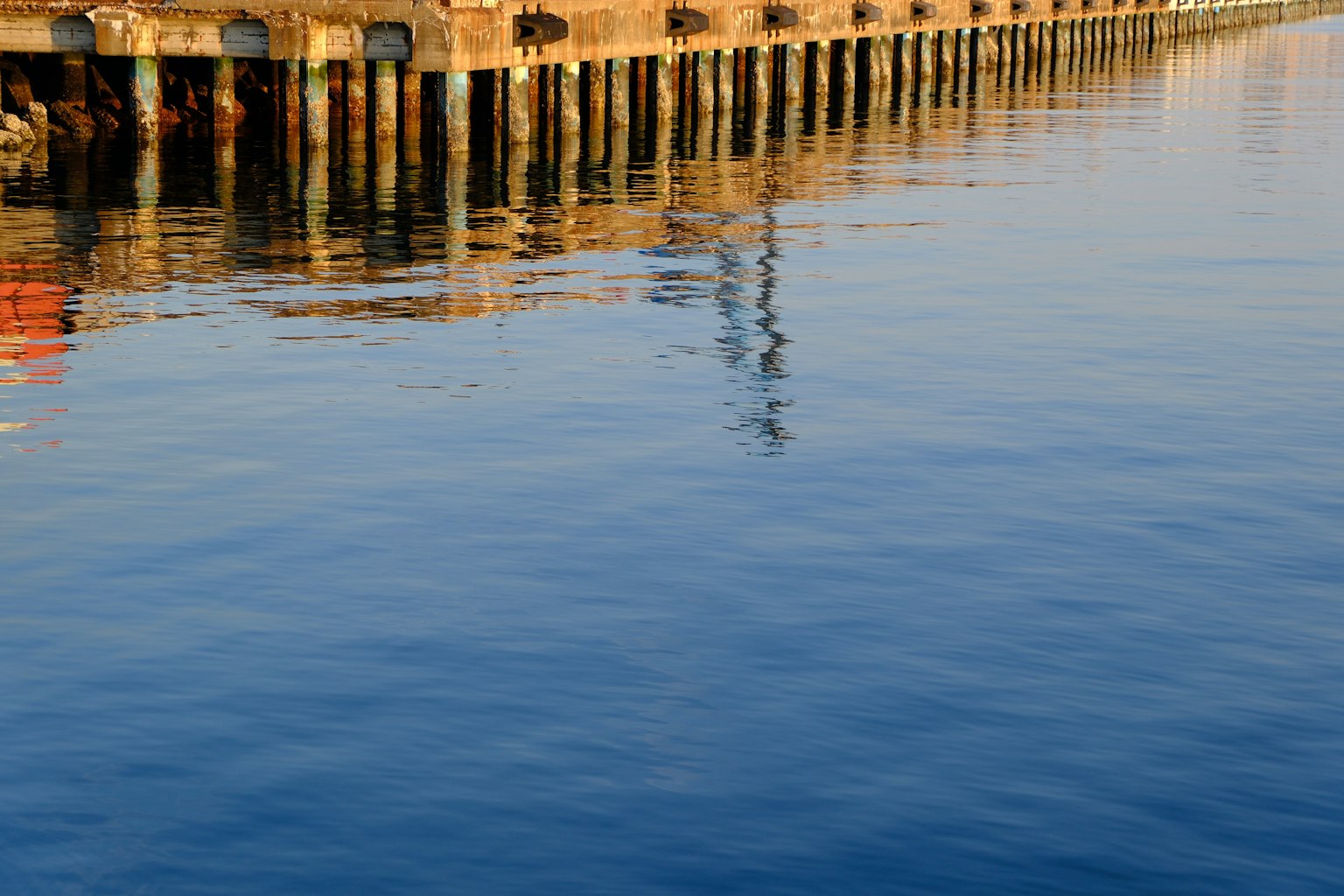 Ruhige Wasseroberfläche, die den Pier und seine Stützen reflektiert