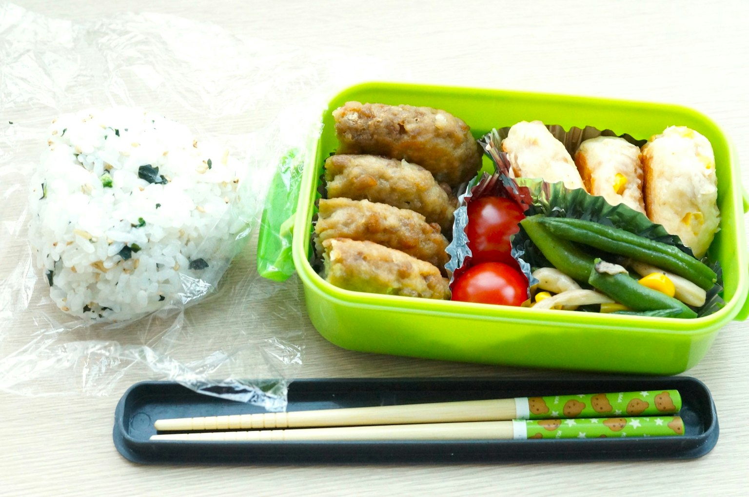 Caja bento verde llena de bolas de arroz y varios acompañamientos