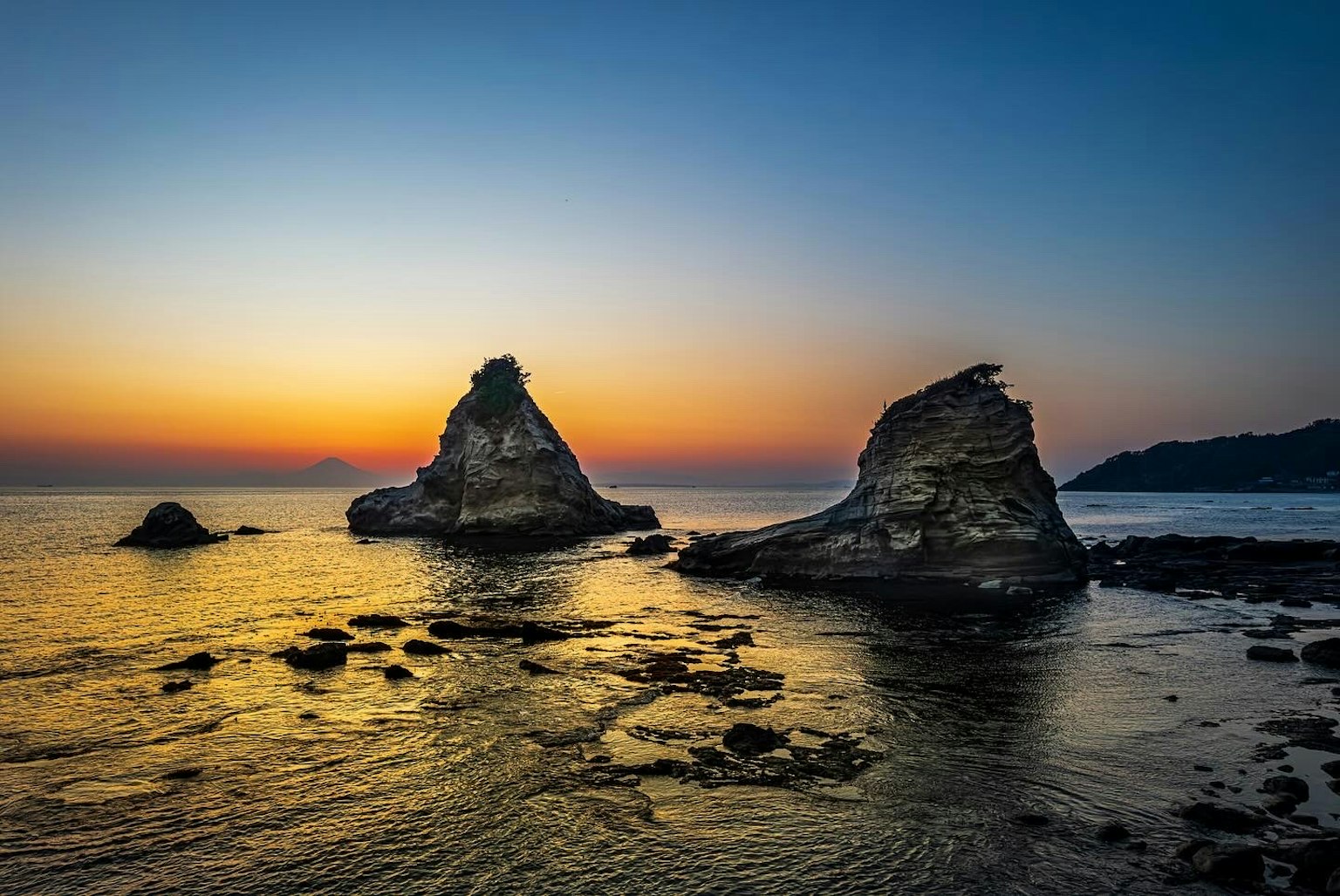 夕焼けの海岸に立つ二つの岩と穏やかな波