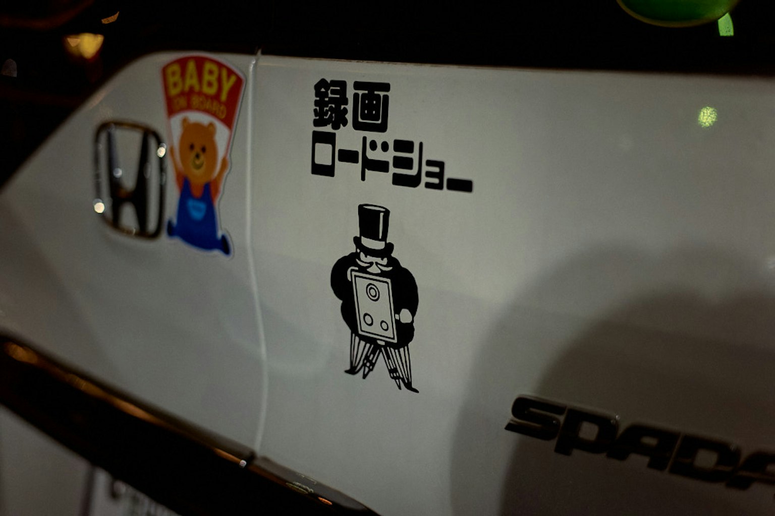 Sticker on the side of a white car featuring a baby character and a man in a top hat