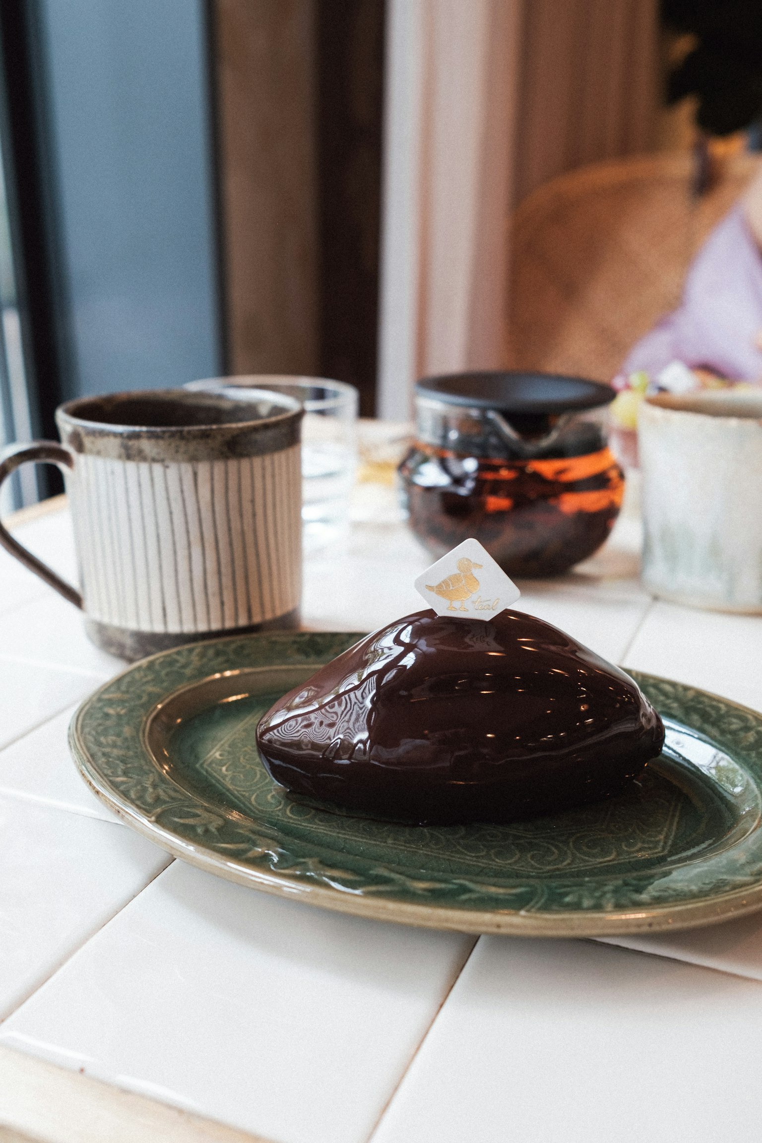 Chocolate cake on a green plate with coffee cup and teapot in background