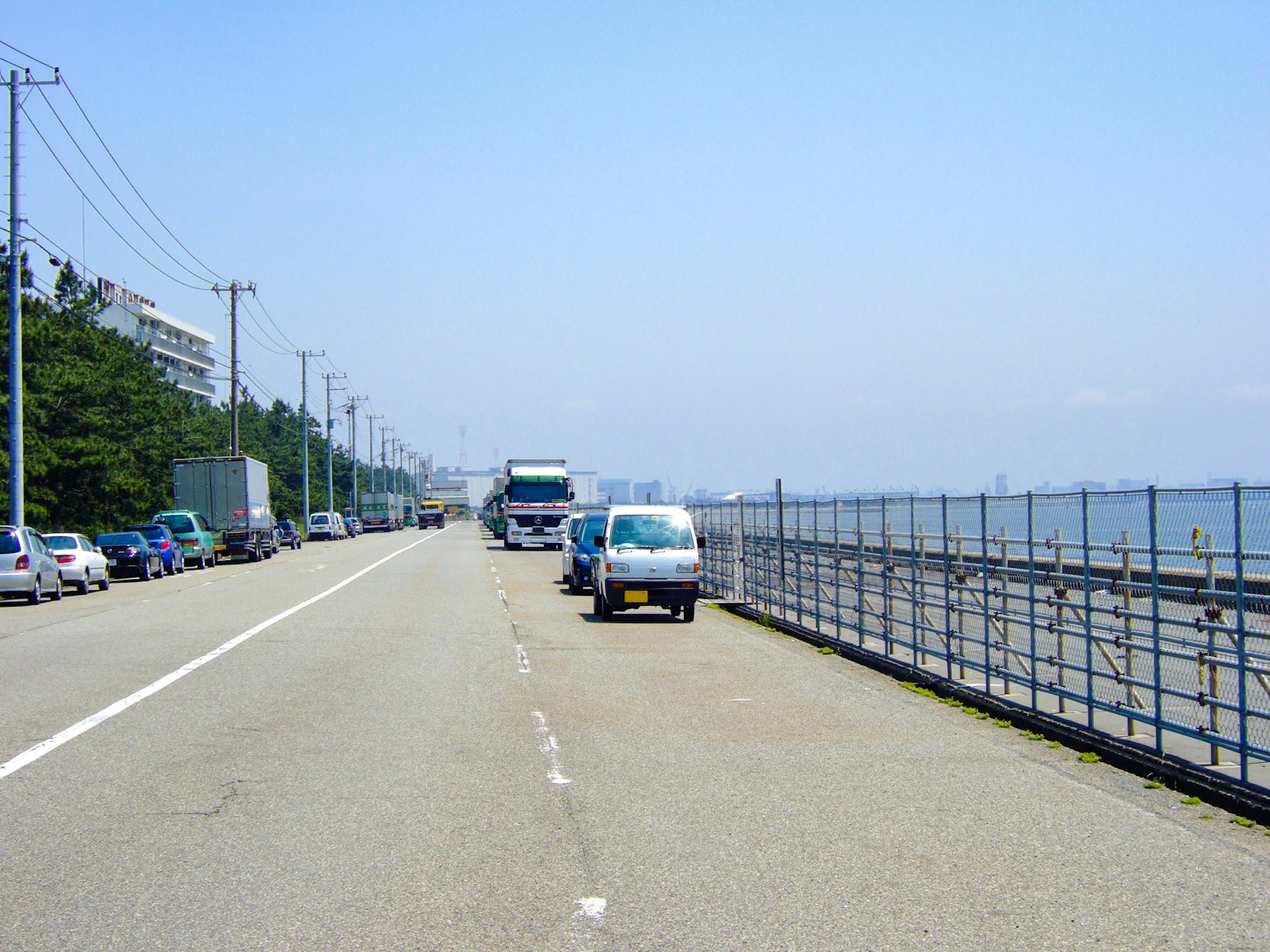 Pemandangan indah jalan di tepi laut dengan mobil terparkir dan langit biru cerah