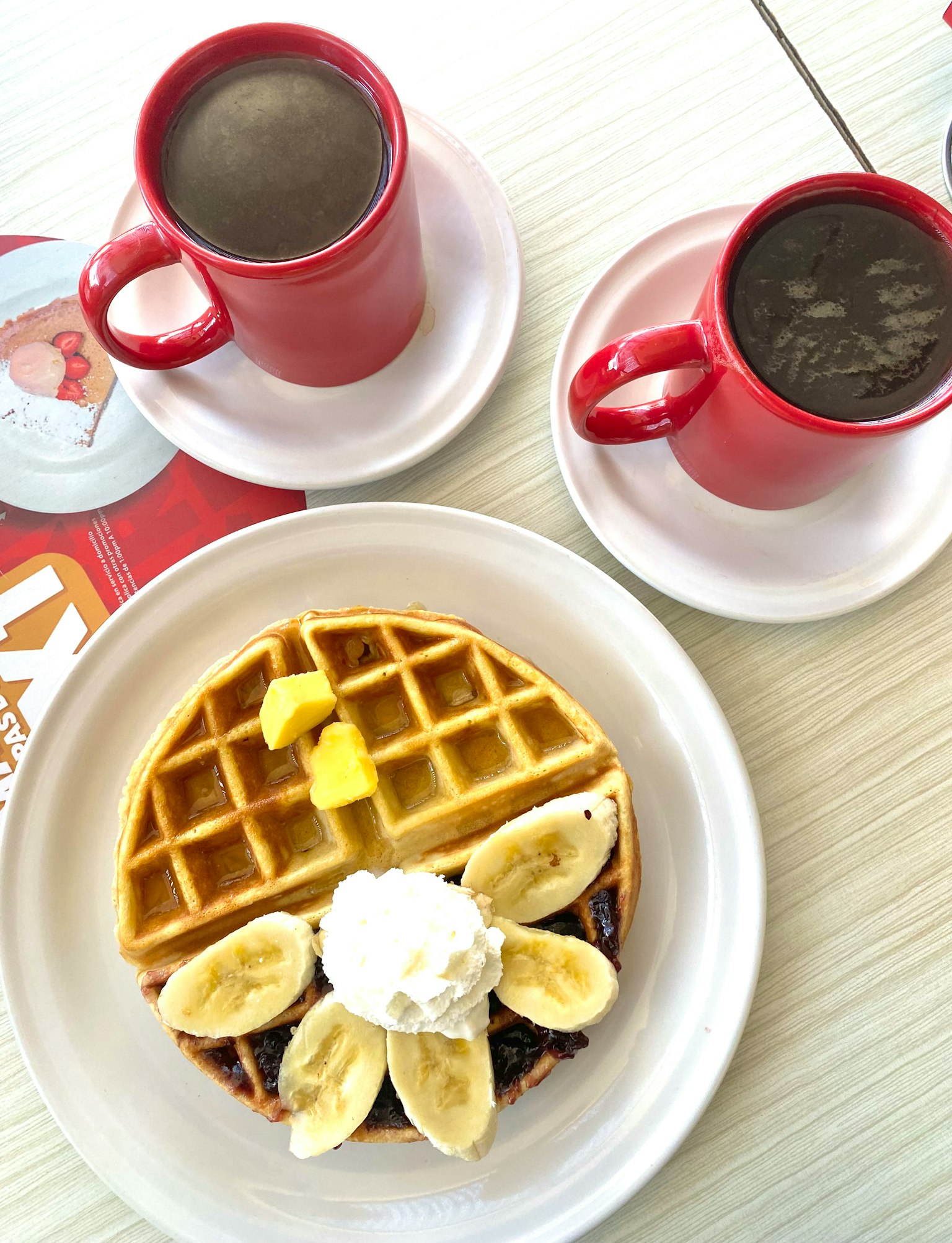 Assiette de gaufre garnie de tranches de banane et de crème fouettée avec deux tasses de café
