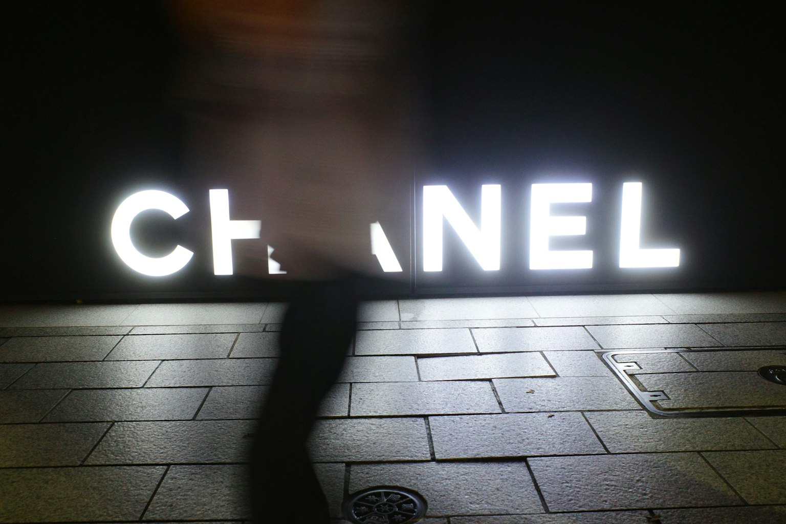 暗い背景に白い光で照らされたCHANELのロゴと人のシルエット