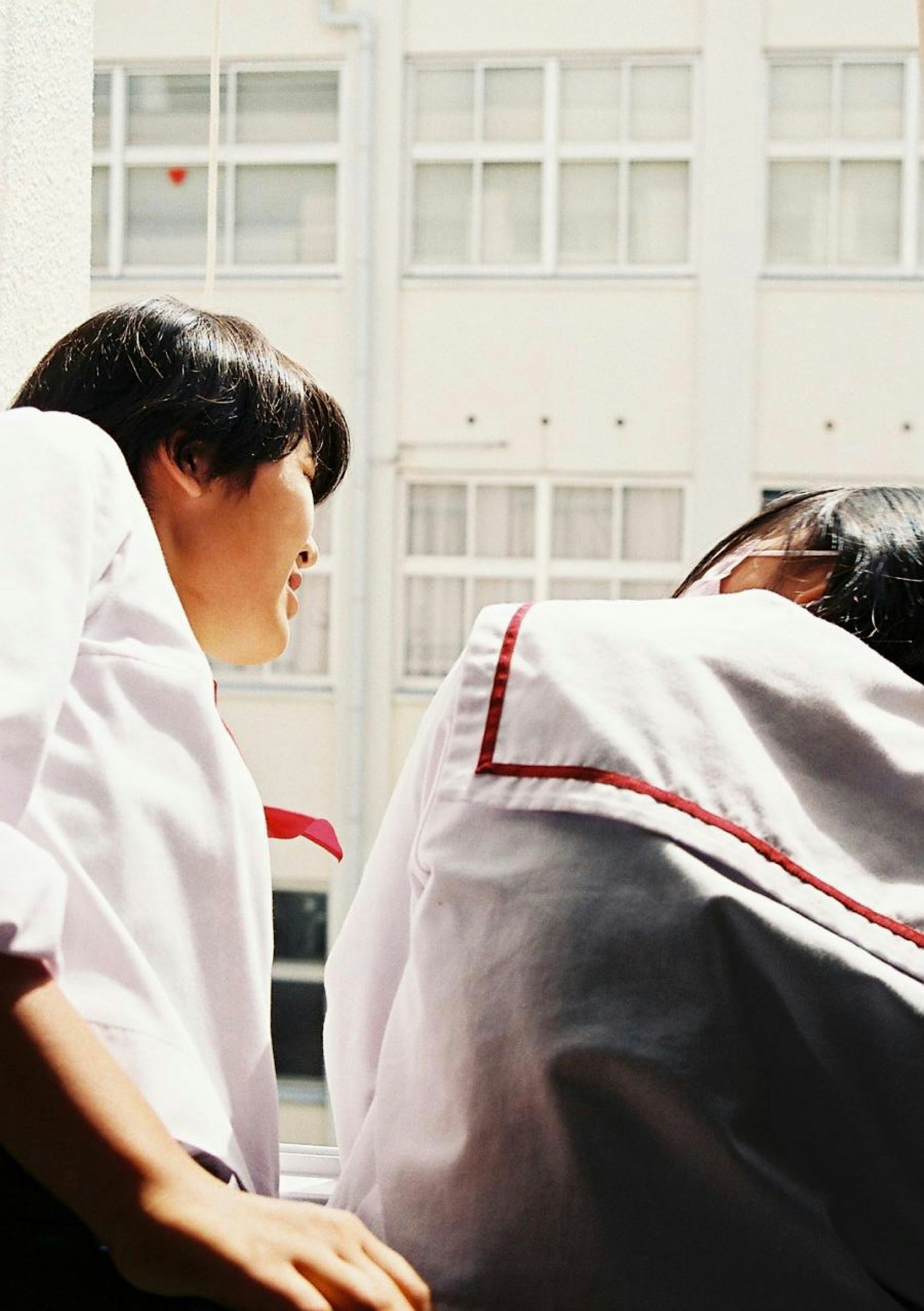 Étudiants regardant par la fenêtre d'une salle de classe portant des chemises blanches et des uniformes à rayures rouges