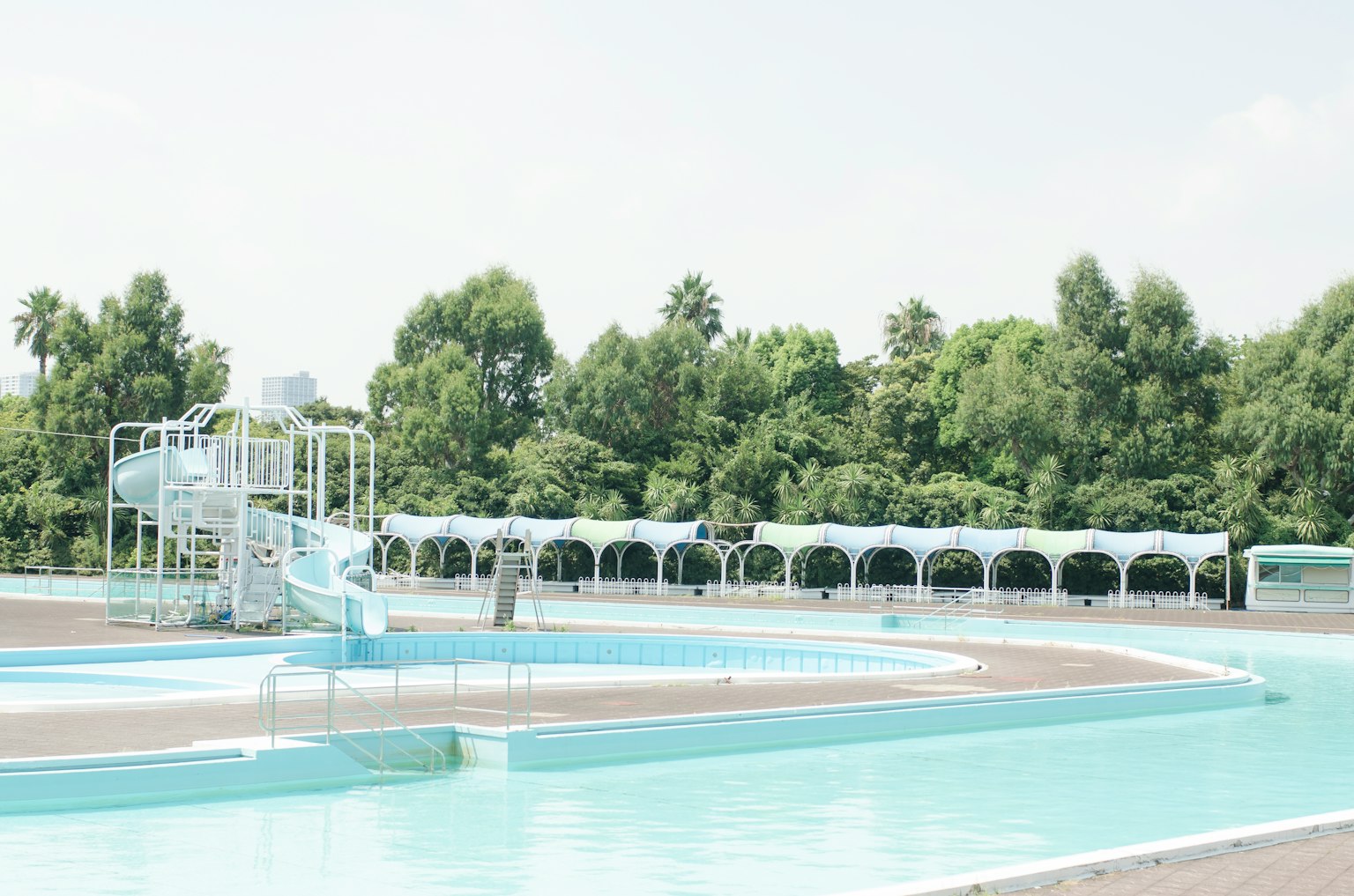 ทิวทัศน์ของสระว่ายน้ำสีน้ำเงินพร้อมสไลด์ที่มีต้นไม้สีเขียวล้อมรอบ