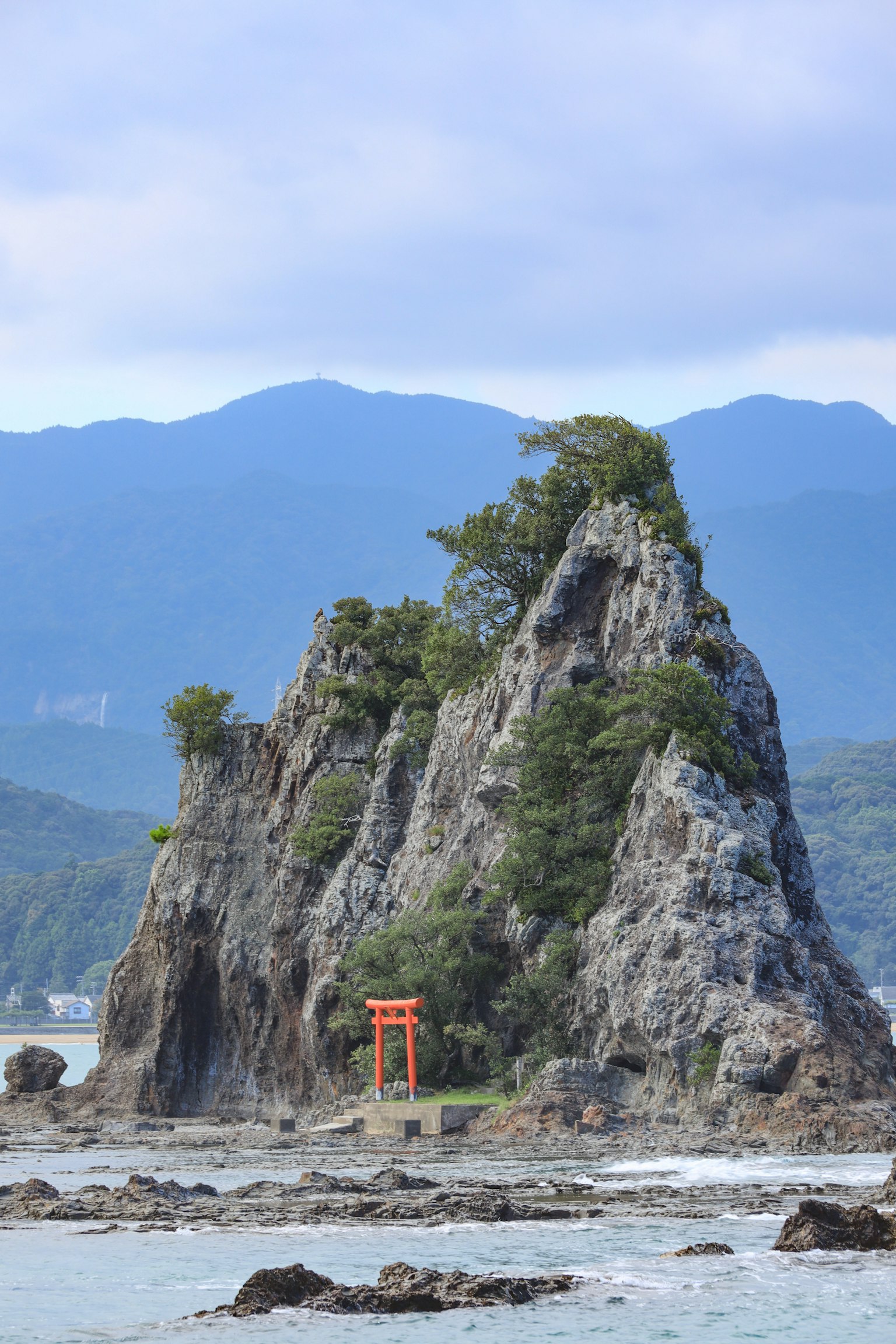 Formasi batu pesisir dengan gerbang torii merah dan vegetasi subur