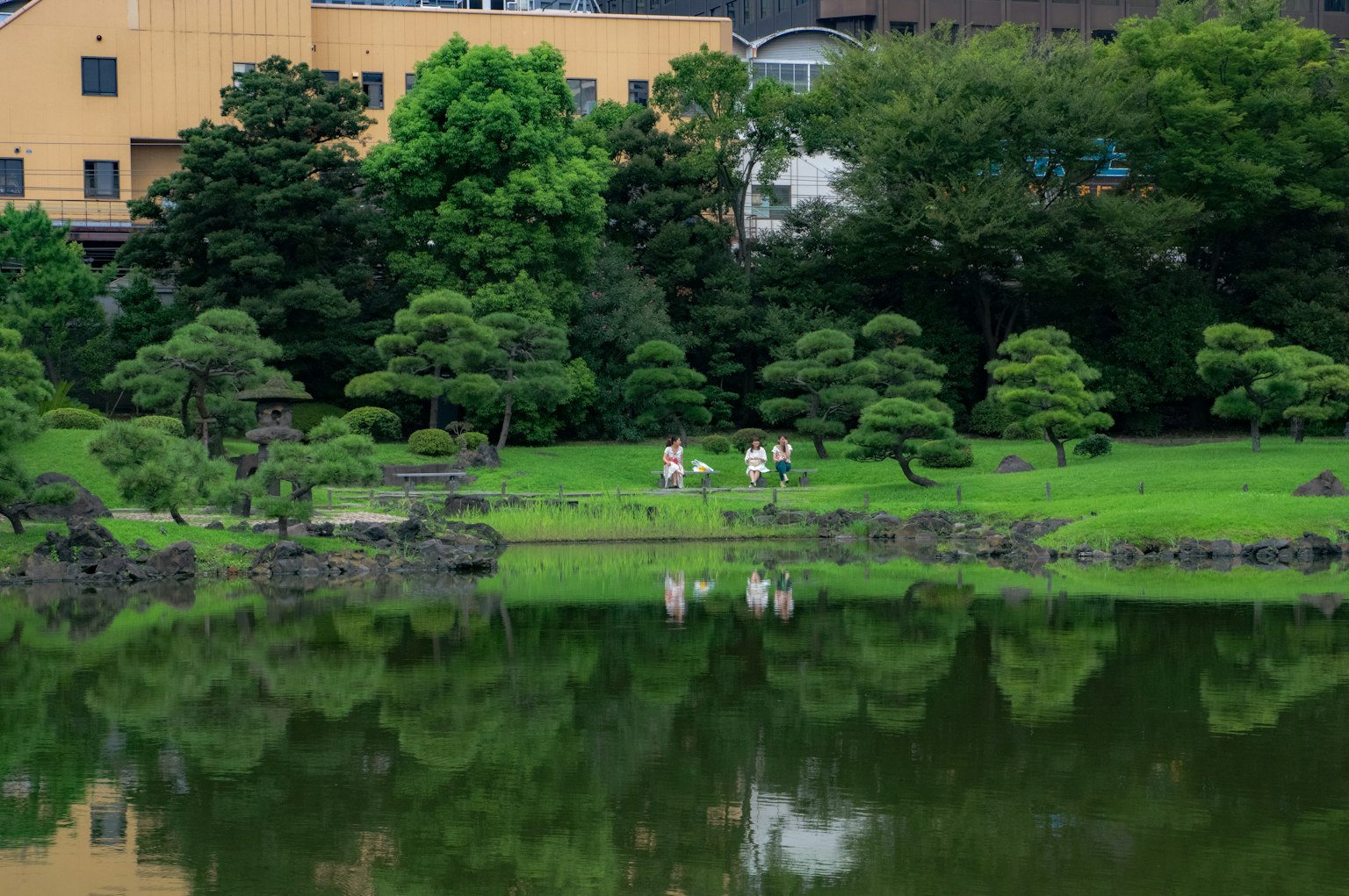 宁静的日本庭园场景，绿色树木和石头在水中倒影，附近聚集着人们