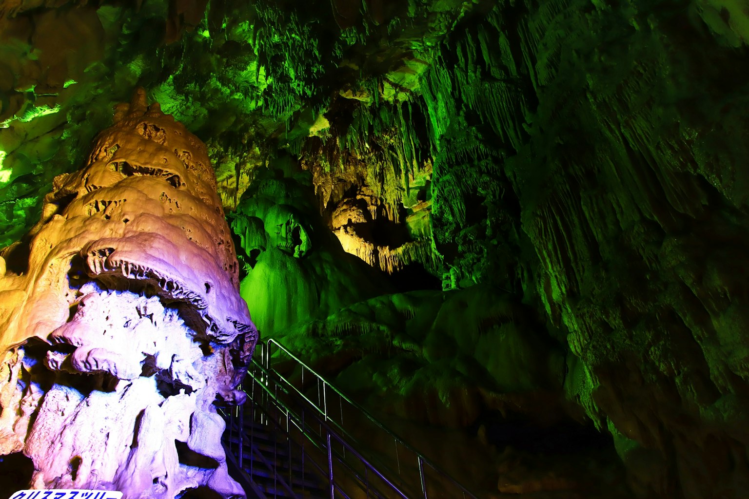 Interior of a cave illuminated with green lighting featuring rock formations and a staircase